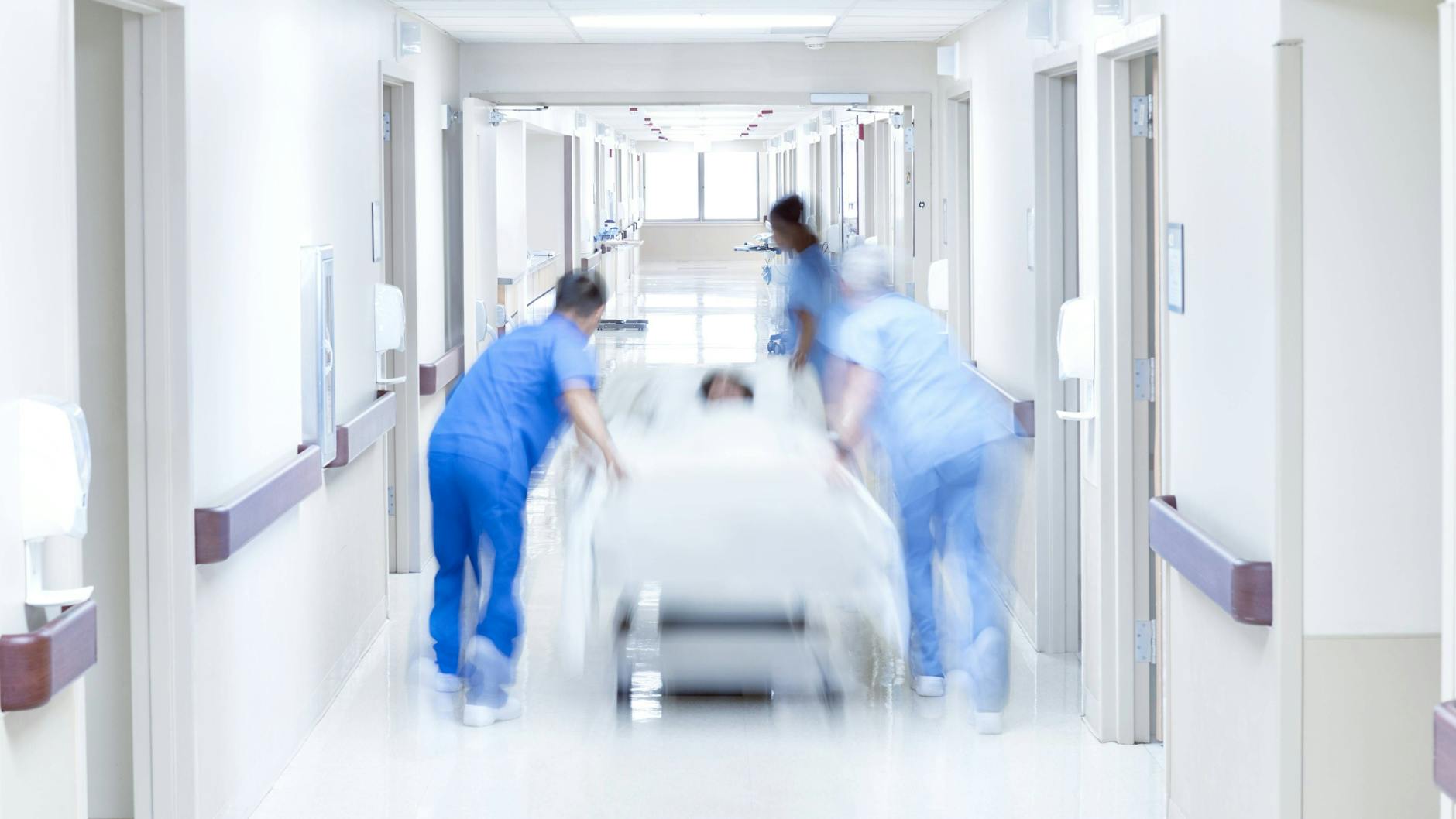 Pflegekräfte schieben eine Frau im Krankenbett durch den Flur einer Klinik (Symbolbild).