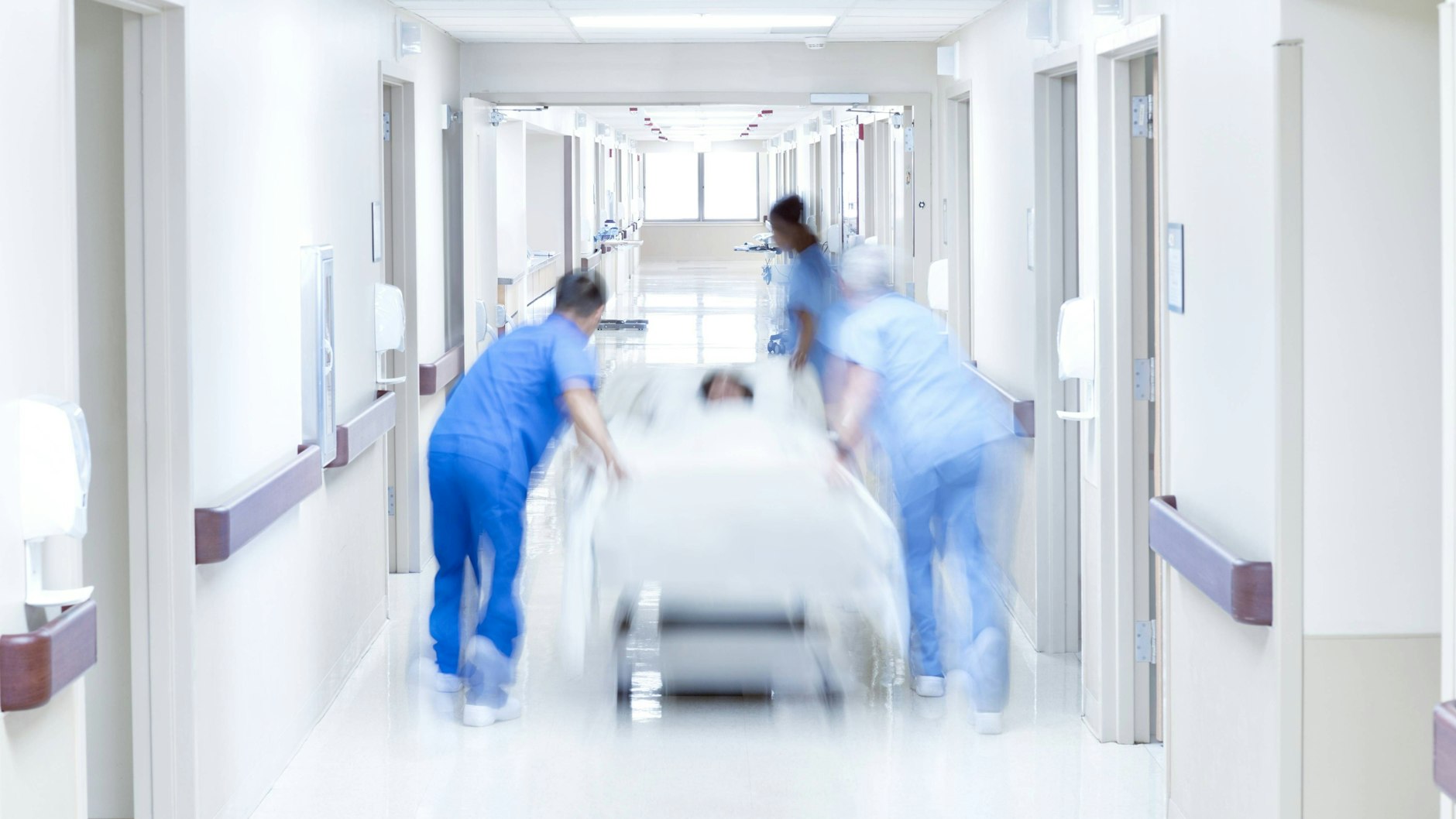 Pflegekräfte schieben eine Frau im Krankenbett durch den Flur einer Klinik (Symbolbild).