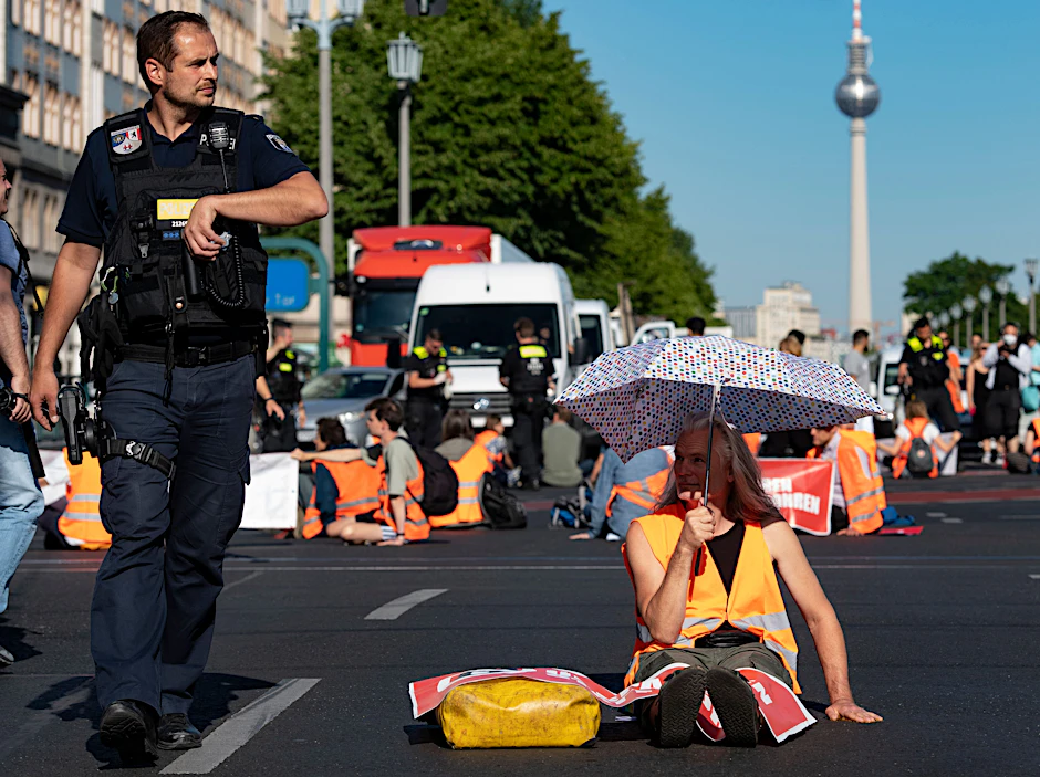 Aktivisten der Letzten Generation blockieren die Fahrbahn in der Karl-Marx-Allee.