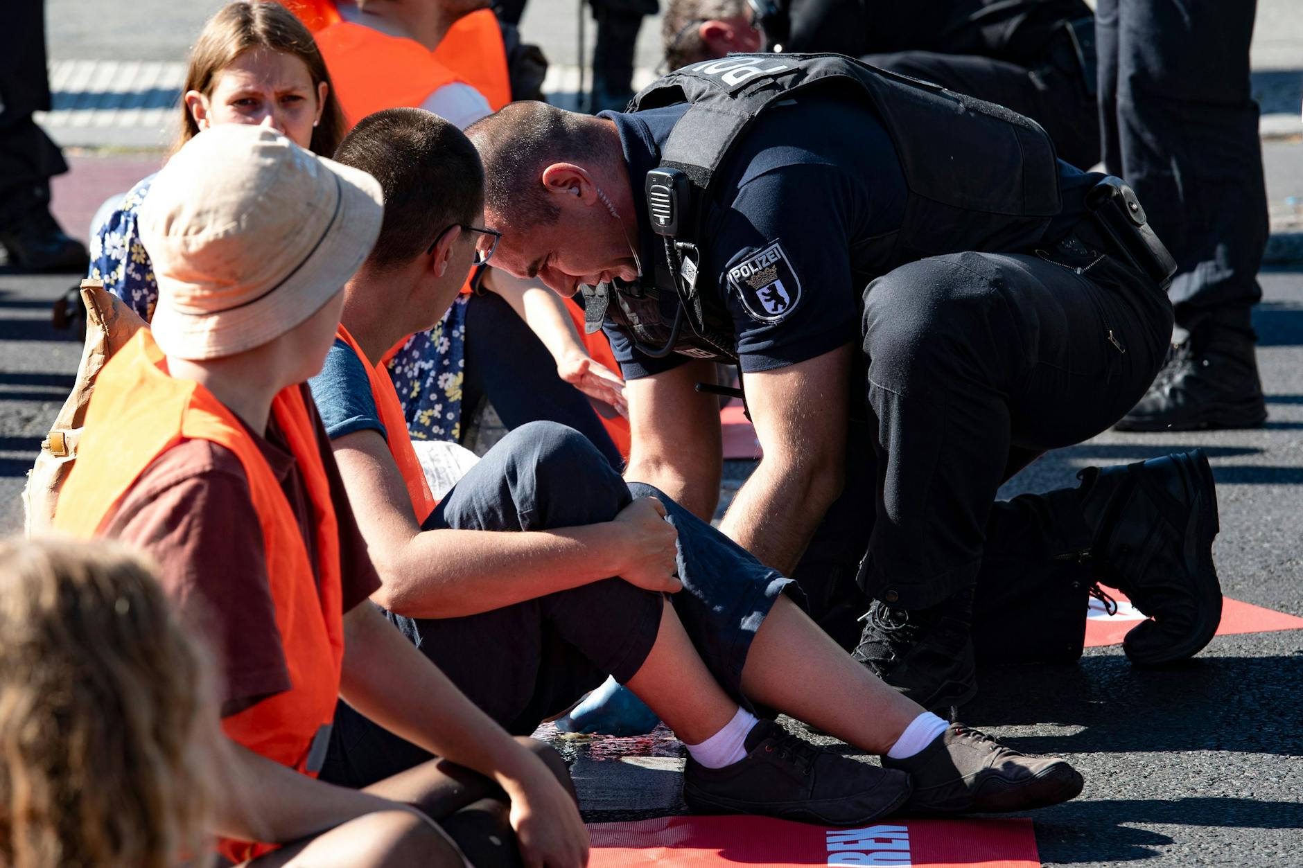 Ein Polizeibeamter löst mit Sonnenblumenöl die festgeklebte Hand eines Klimaschutz-Demonstranten der Gruppe „Letzte Generation“