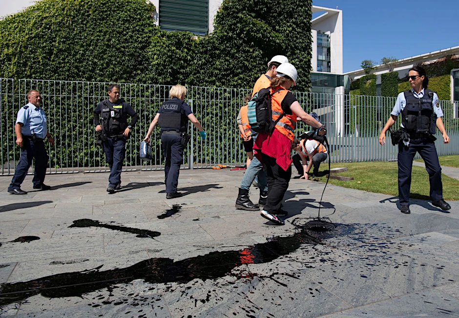 Klimaschutz-Demonstranten verschütten eine ölartige Flüssigkeit auf den Boden.  