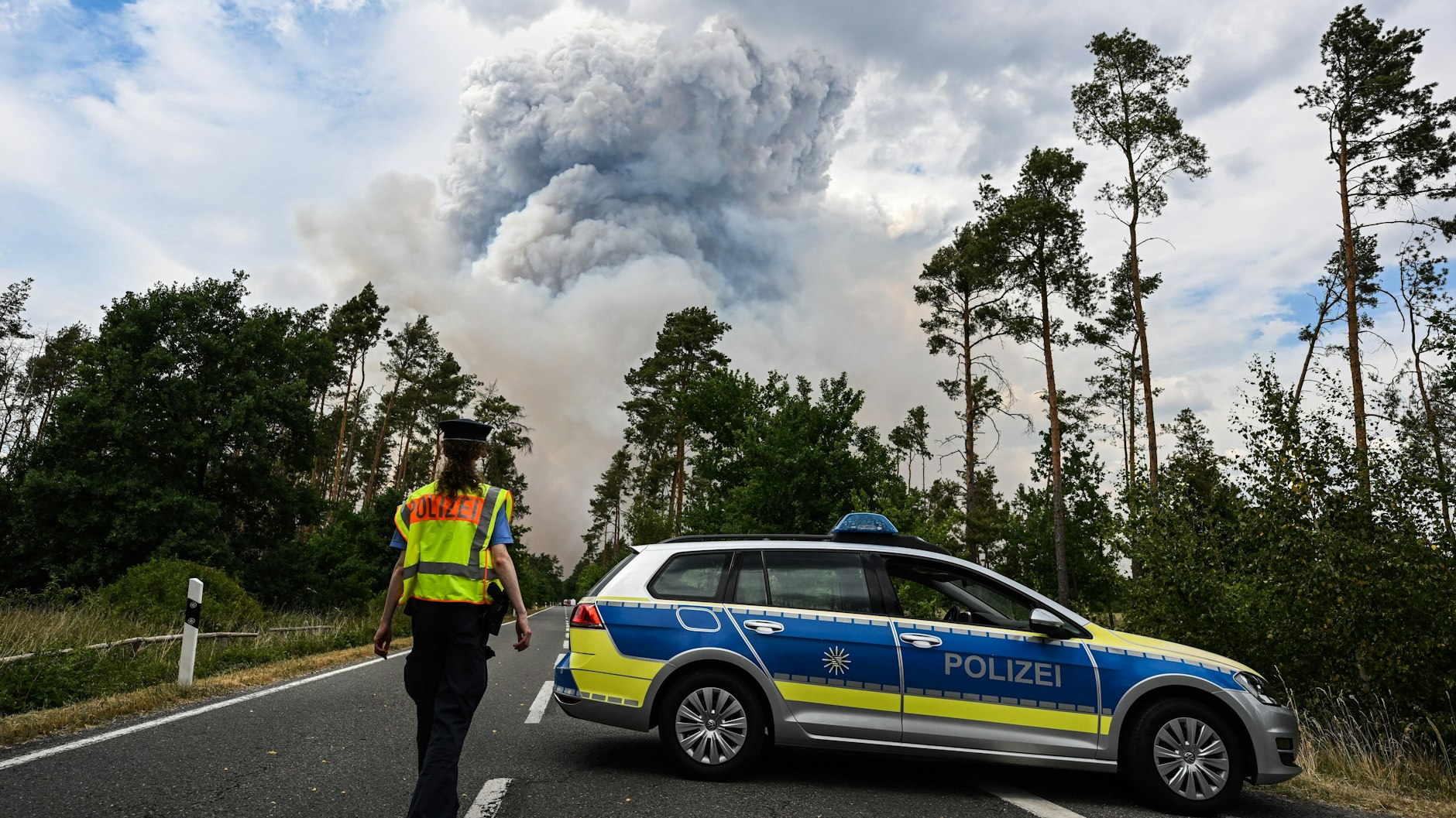 Ein Polizeiauto sperrt die Straße zum Waldbrand-Gebiet ab.