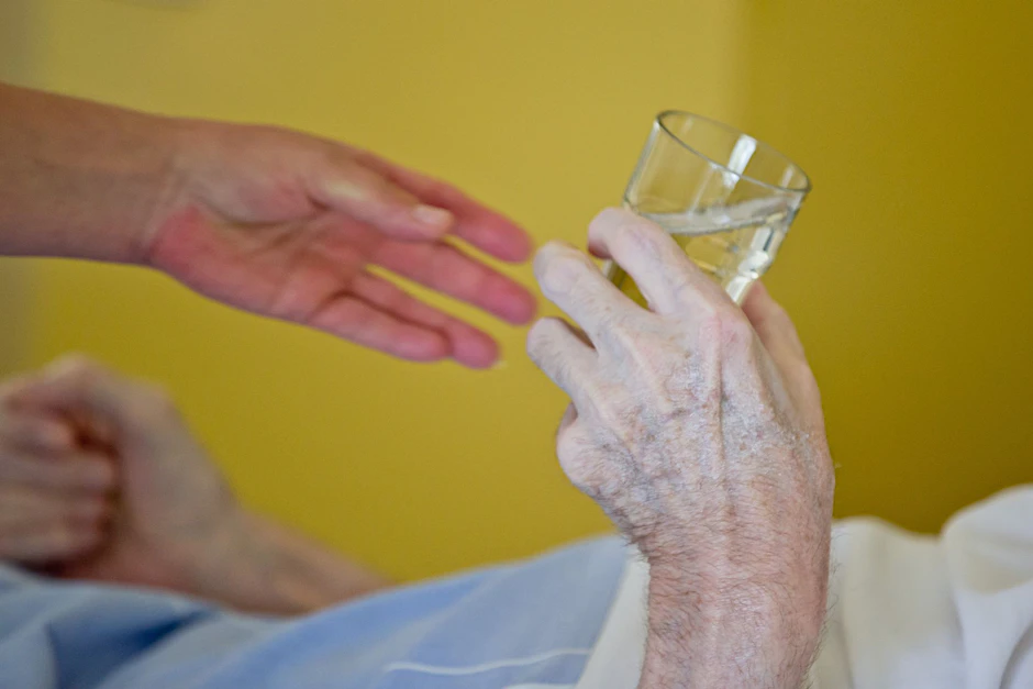 ARCHIV - Eine Krankenpflegerin reicht einem Patienten ein Glas Wasser.  