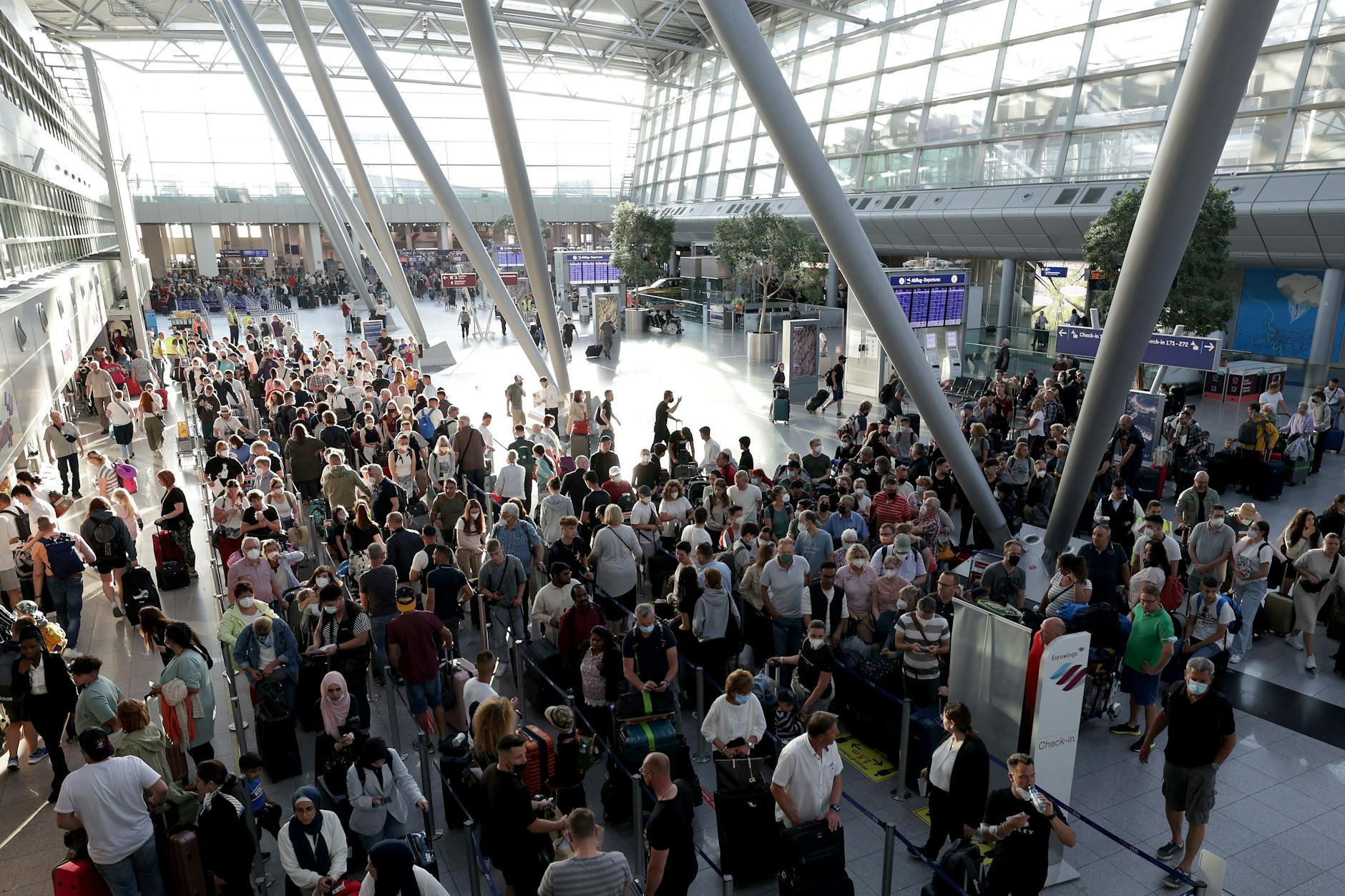 Passagiere drängeln sich in langen Schlangen vor den Schaltern im Flughafen Düsseldorf und warten auf die Abfertigung.