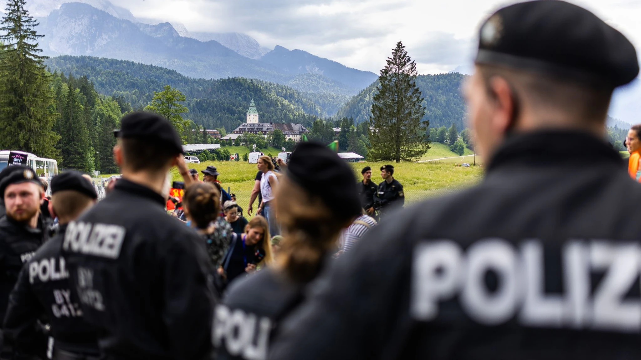 Eine Gruppe von Polizisten steht in Sichtweite von Schloss Elmau (im Hintergrund) und beobachtet eine Demonstration.
