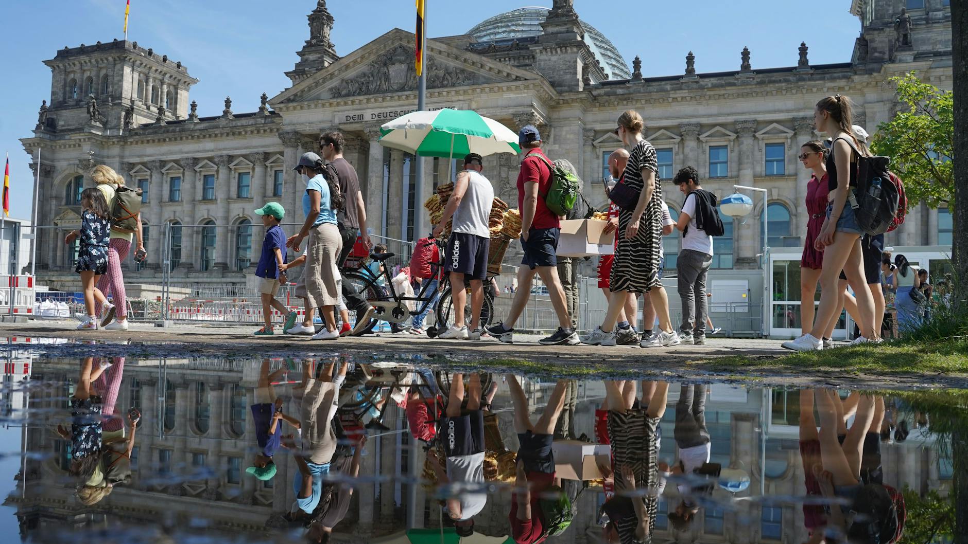 Zahlreiche Menschen gehen bei strahlendem Sonnenschein am Reichstagsgebäude vorbei. Die hohen Temperaturen lösten bei manchem Kreislaufprobleme aus.