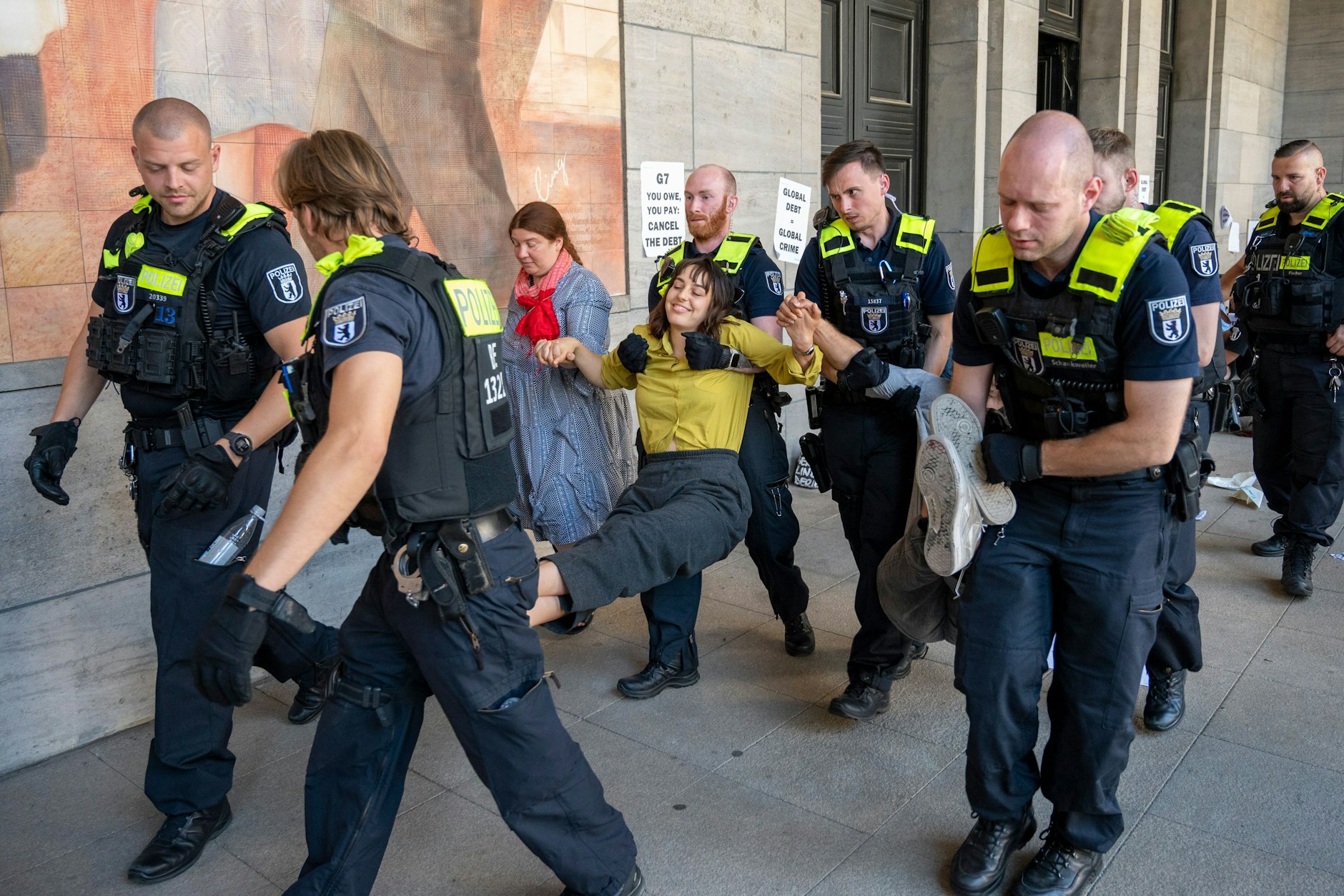 Polizisten tragen Aktivisten, die aneinanderkleben. Die Aktivisten hatten sich vor dem Eingang des Finanzministeriums festgeklebt und demonstrieren für einen globalen Schuldenerlass und Klimagerechtigkeit.