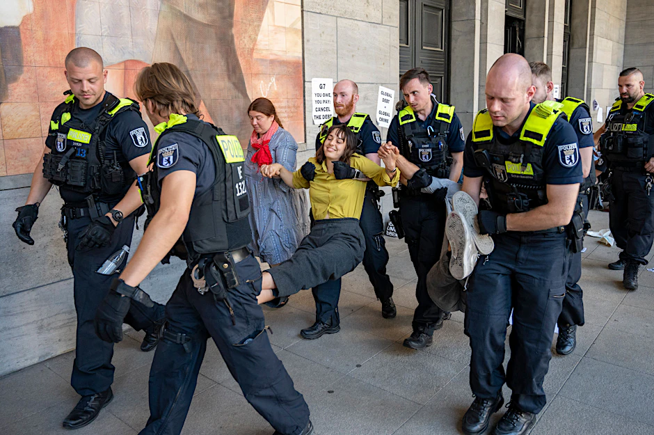 Polizisten tragen Aktivisten, die aneinanderkleben. Die Aktivisten hatten sich vor dem Eingang des Finanzministeriums festgeklebt und demonstrieren für einen globalen Schuldenerlass und Klimagerechtigkeit.