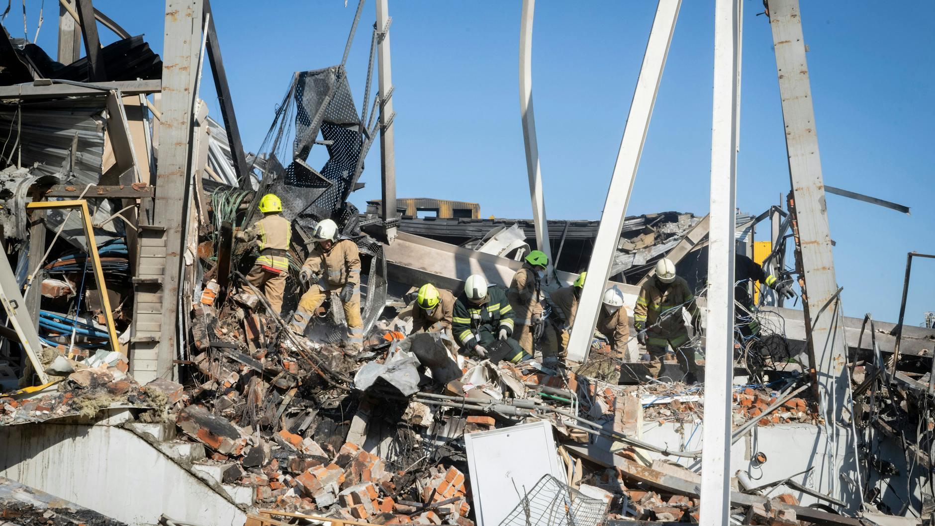 Feuerwehrleute arbeiten daran, Trümmer eines nach einem Raketenangriff in Krementschuk abgebrannten Einkaufszentrums zu beseitigen.