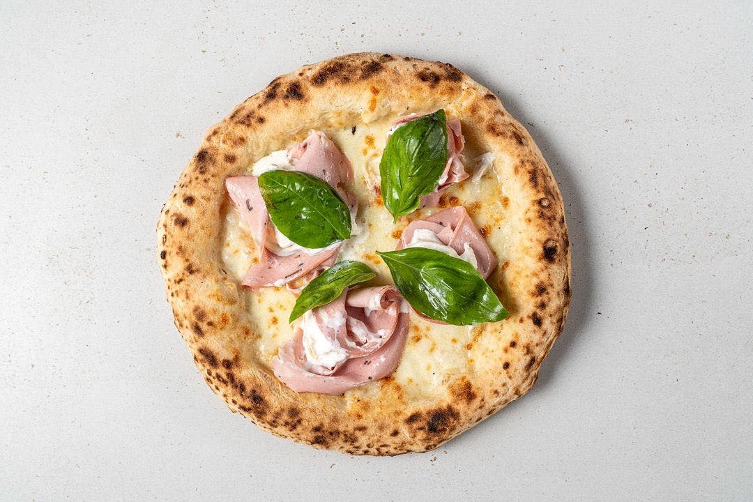 Die sommerliche Pizza ist wunderschön, die Farben wie ein Gemälde: Ein dicker, von Beige ins Dunkelgold spielende Rand, klar neapolitanisch geschwollen mit einigen Blasen.