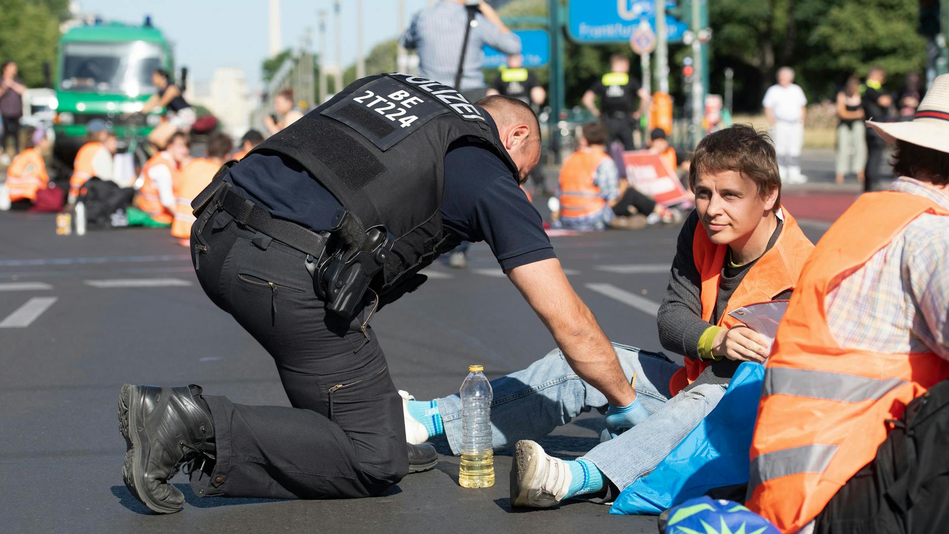Ein Polizist löst Demonstranten der Letzten Generation mit Speiseöl von einer Kreuzung.