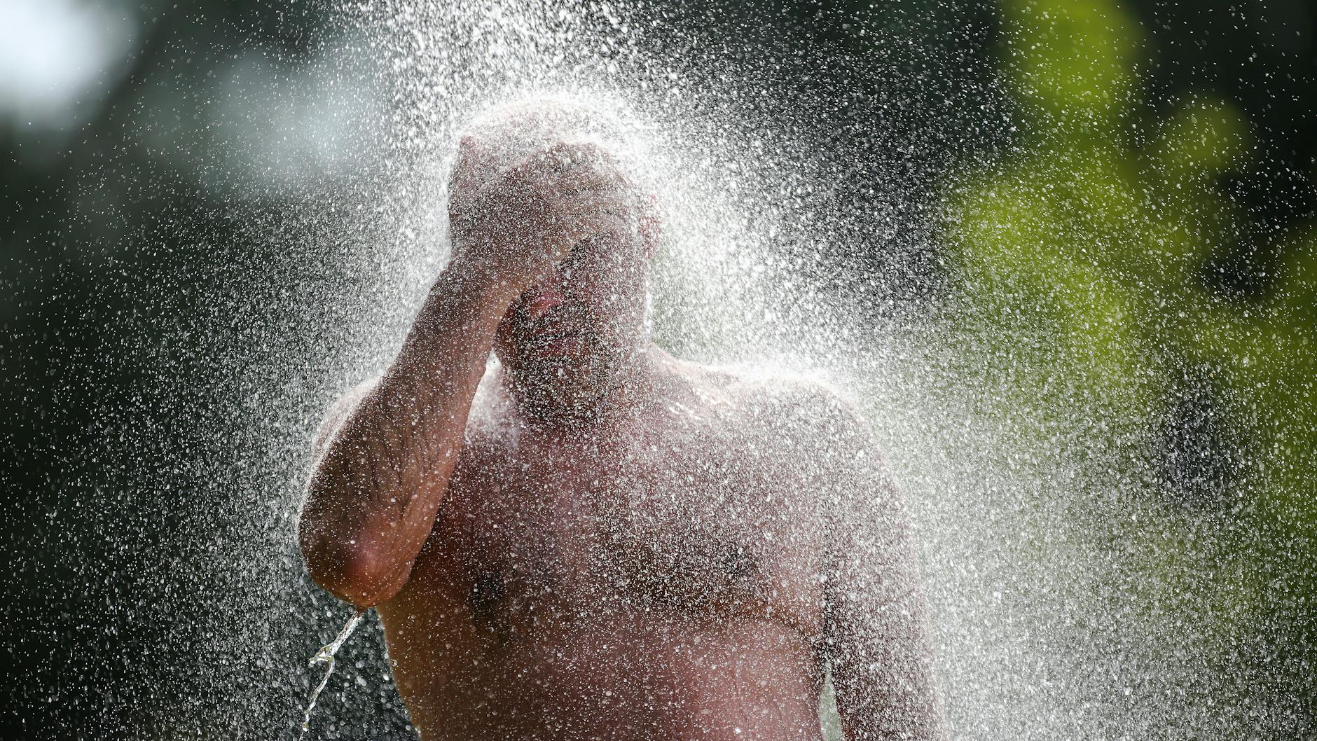 Ein Mann steht an einem Badesee unter einer Dusche.
