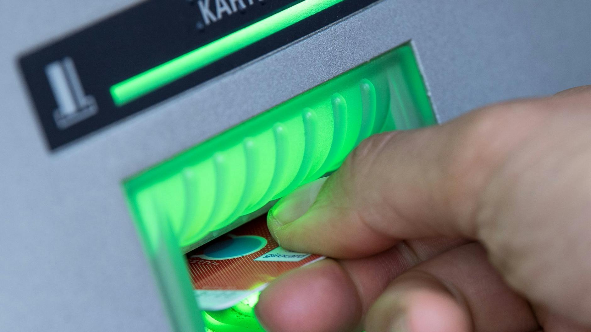 Eine Bankkarte steckt in einem leuchtenden Schlitz am Bankautomaten.