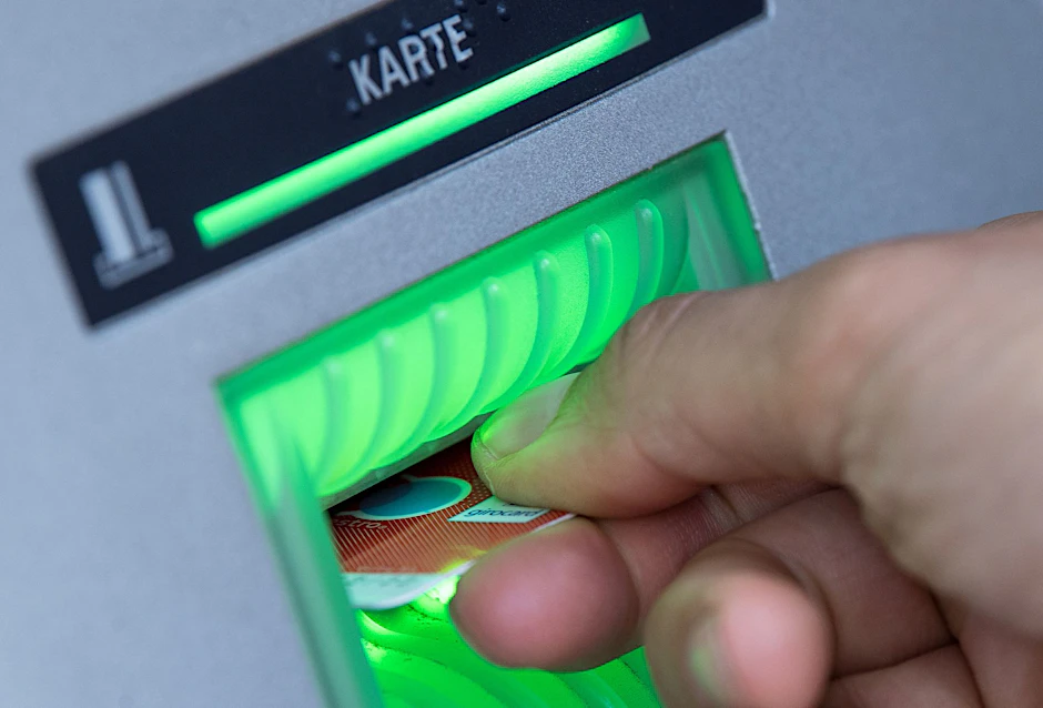 Eine Bankkarte steckt in einem leuchtenden Schlitz am Bankautomaten.