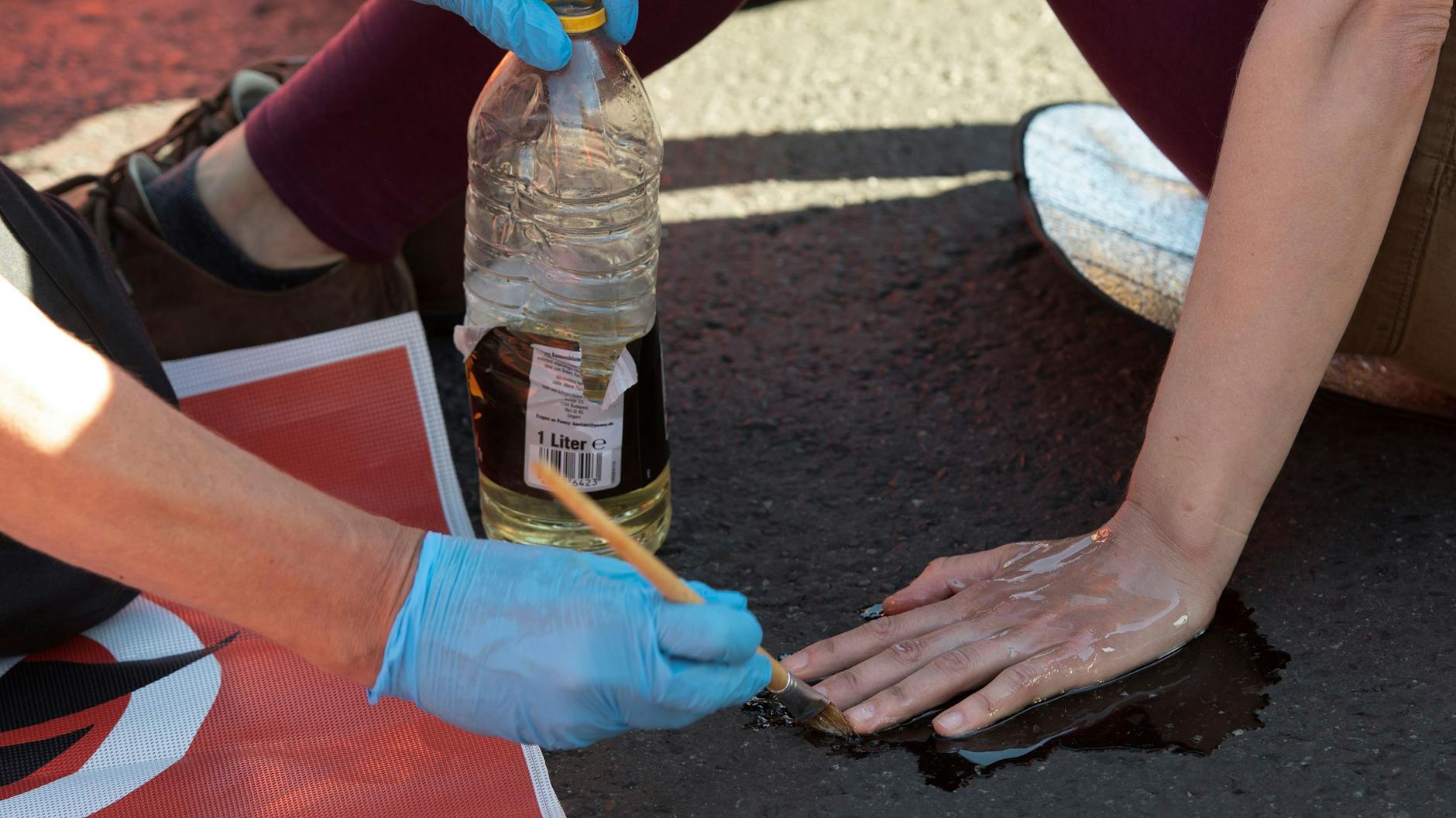 Ein Polizeibeamter löst mit Sonnenblumenöl die festgeklebte Hand eines Klimaschutz-Demonstranten der Gruppe „Letzte Generation“ vom Asphalt. (Archivbild)