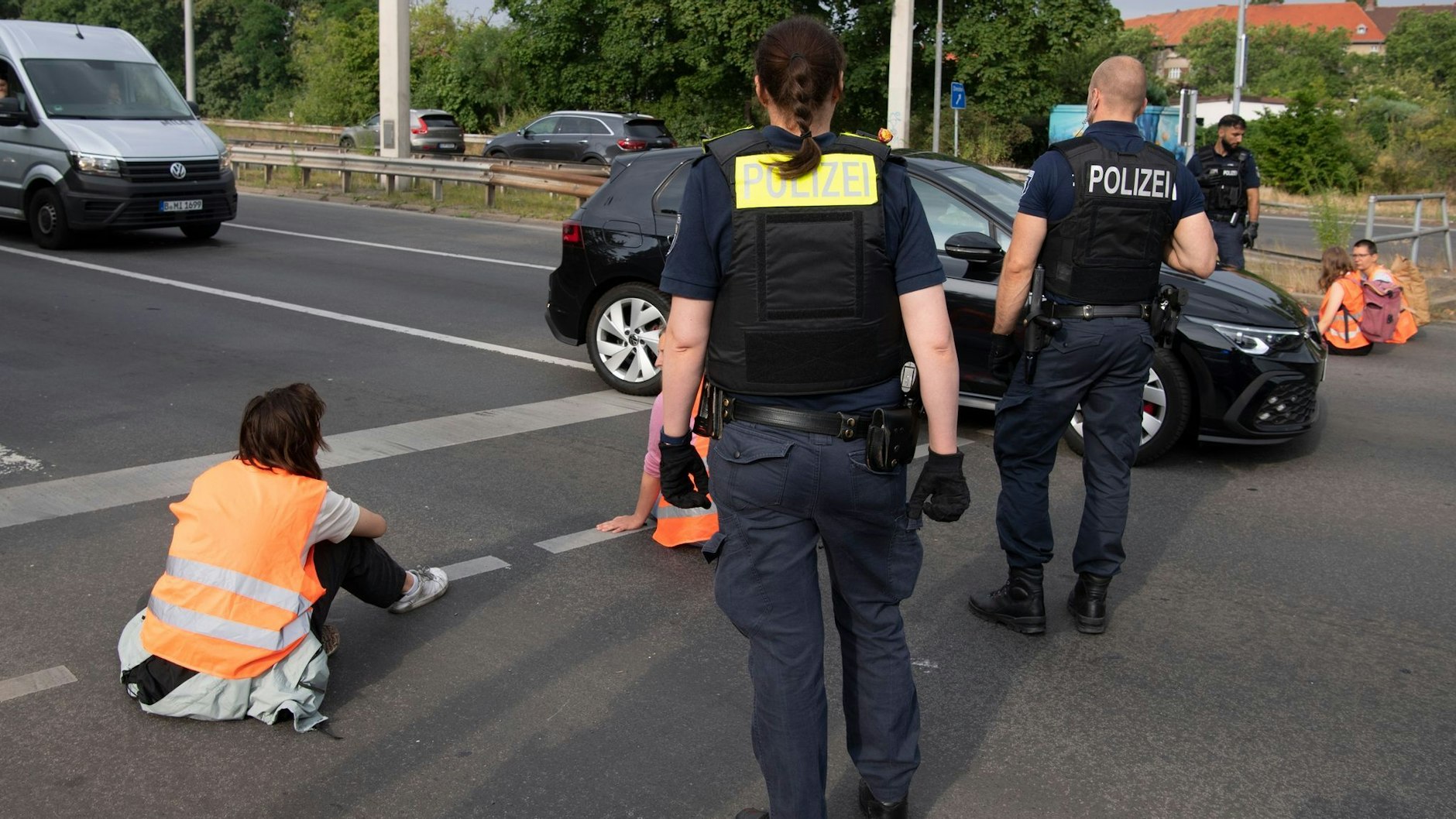 Polizeibeamte stehen bei den Demonstranten der Gruppe „Letzte Generation“ auf einer Kreuzung.