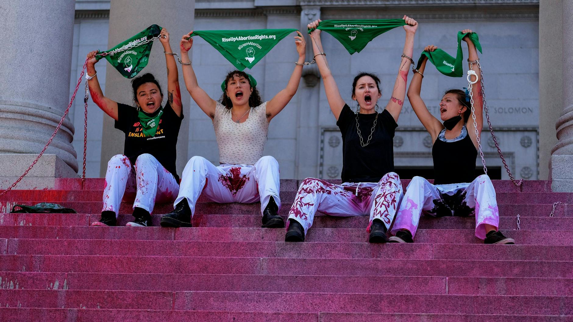 Proteste in den USA: Vier Personen sitzen auf einer Treppe, unter ihnen fließt Kunstblut.