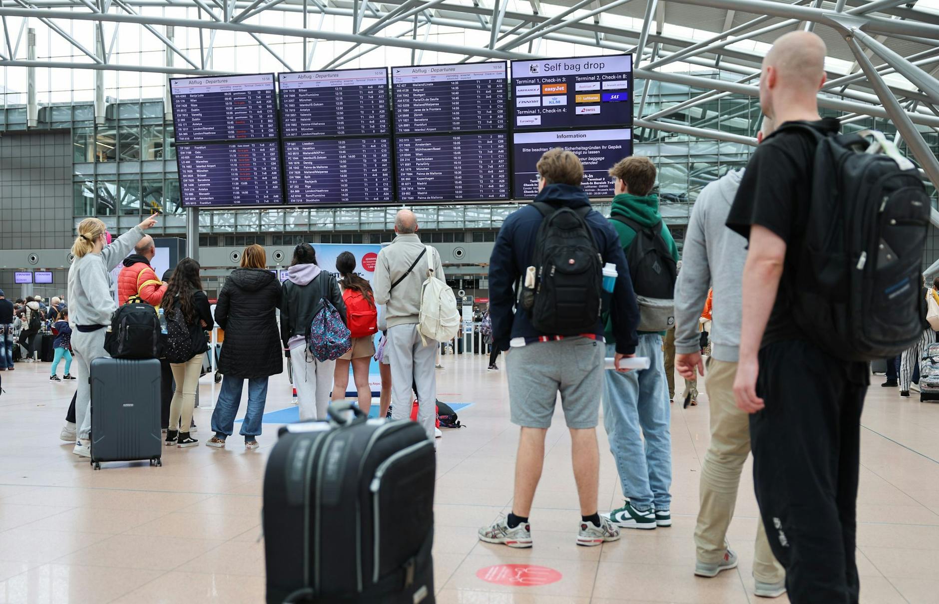 Flugreisende stehen unter den Anzeigetafeln und vor den Check-in-Schaltern am Airport Hamburg.
