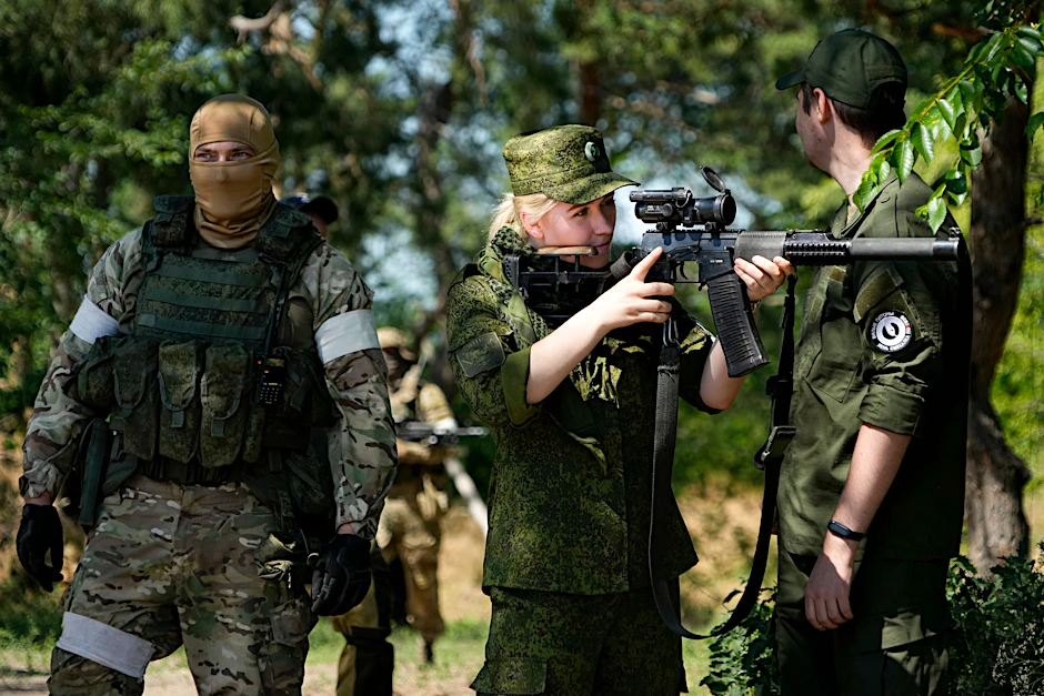 Eine Soldatin der russischen Armee blickt durch ein Scharfschützenzielfernrohr, während sie und andere Soldaten eine Gruppe ausländischer Journalisten bewachen.