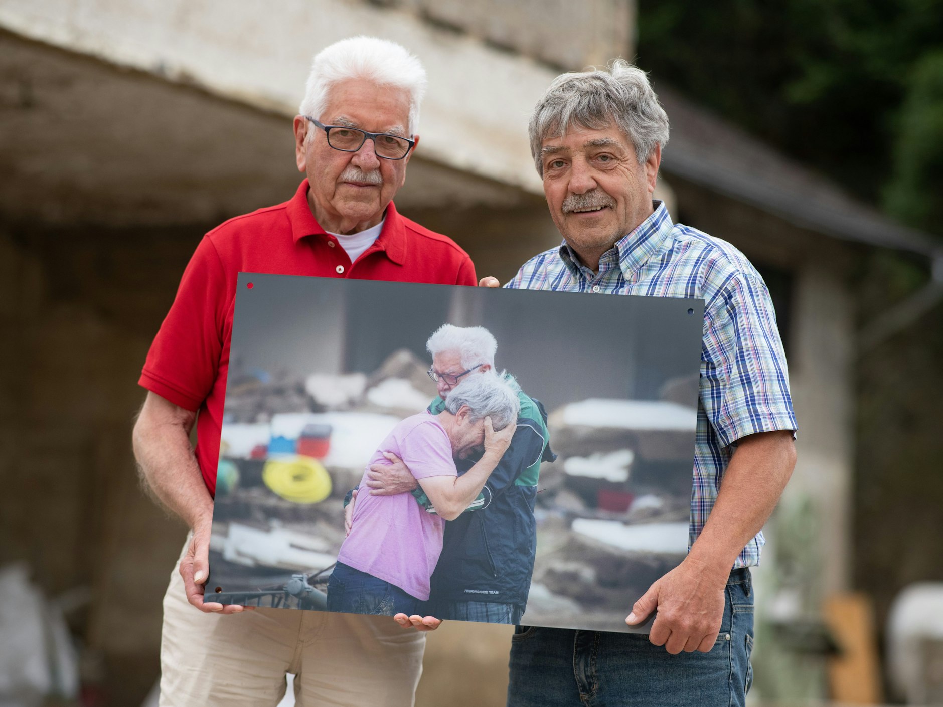 Gerd und Bernd Gasper (r.) stehen vor den Trümmern Elternhauses in Altenahr-Altenstadt. Das Foto in ihren Händen zeigt sie nach der tödlichen Flutwelle vor einem Jahr.