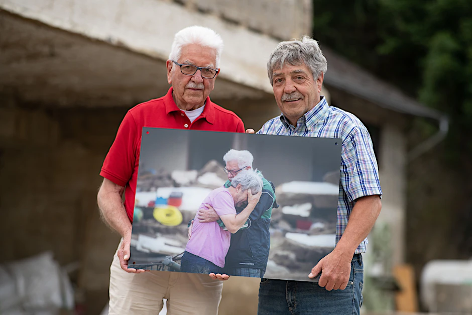 Gerd und Bernd Gasper (r.) stehen vor den Trümmern Elternhauses in Altenahr-Altenstadt. Das Foto in ihren Händen zeigt sie nach der tödlichen Flutwelle vor einem Jahr.