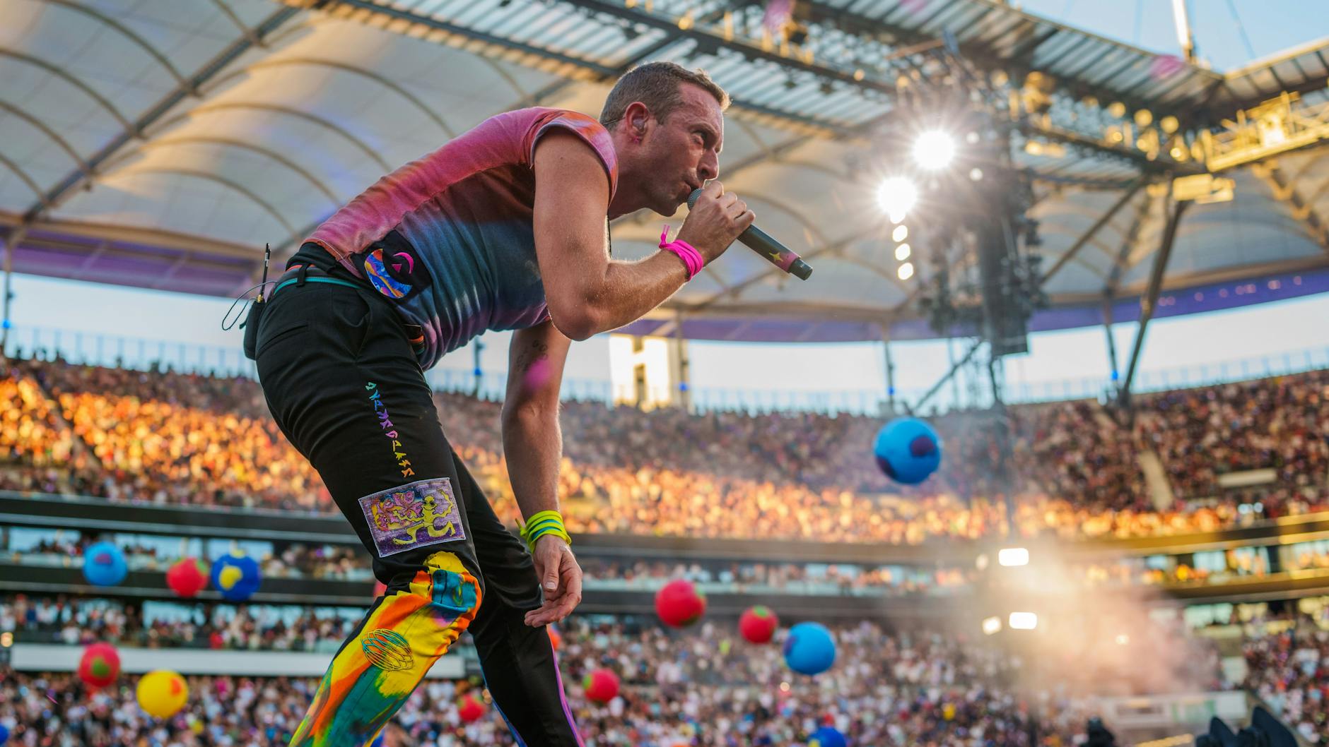 Chris Martin von Coldplay in quietschbunten Hosen und mit Planeten oder Luftballons im Hintergrund. Im Berliner Olympiastadion wird die Band am 12. und 13. Juli zwei weitere Konzerte geben.