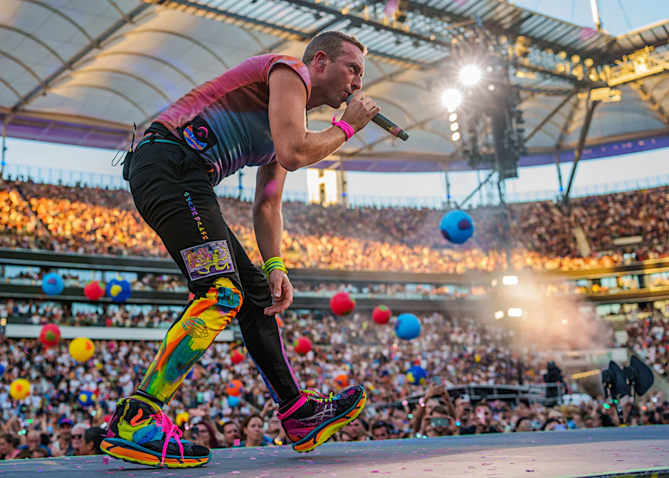 Chris Martin von Coldplay in quietschbunten Hosen und mit Planeten oder Luftballons im Hintergrund. Im Berliner Olympiastadion wird die Band am 12. und 13. Juli zwei weitere Konzerte geben.