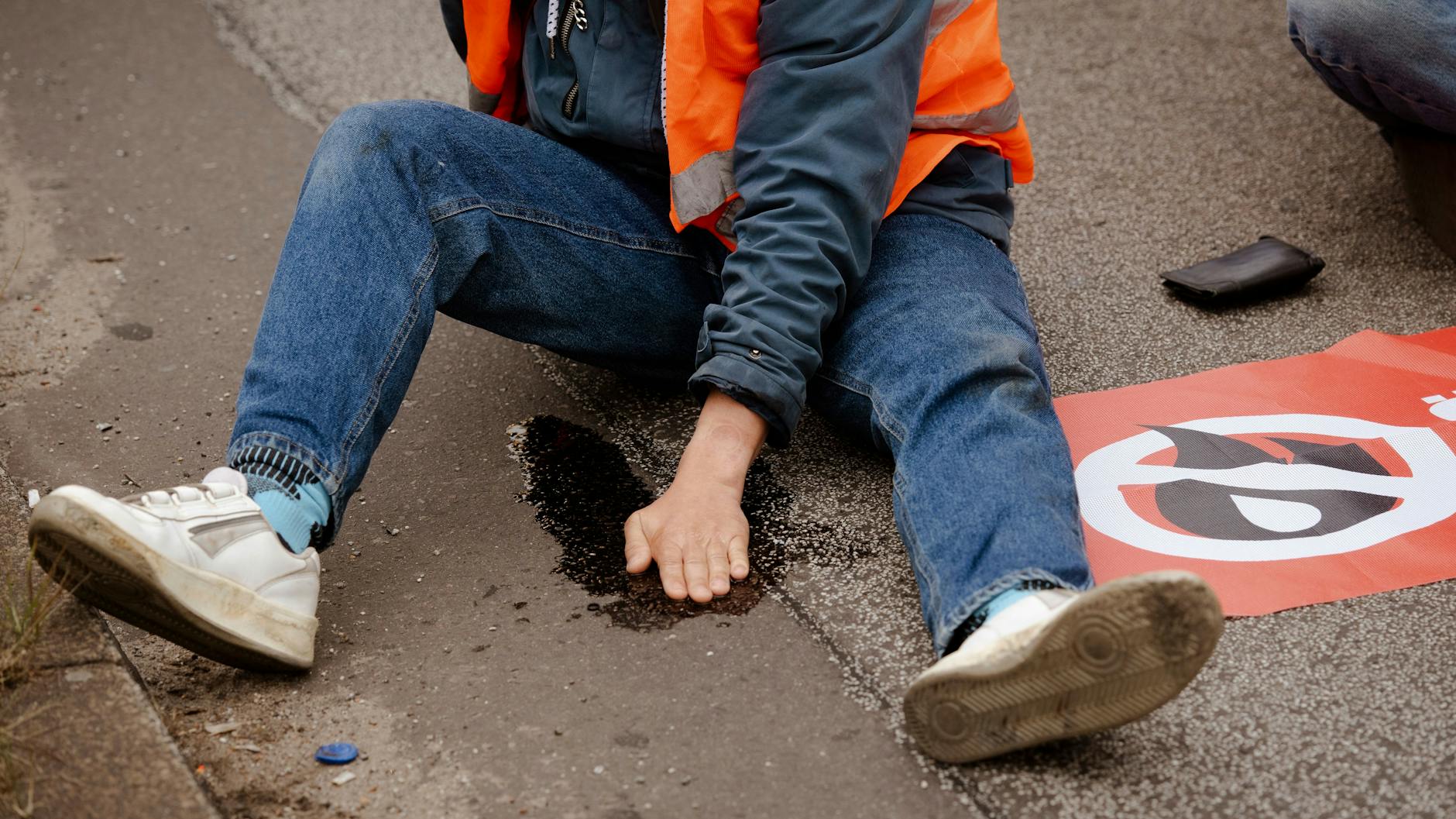 Ein Mitglied der Klimaschutz-Gruppe sitzt mit einer festgeklebten Hand auf dem Asphalt. (Symbolbild)