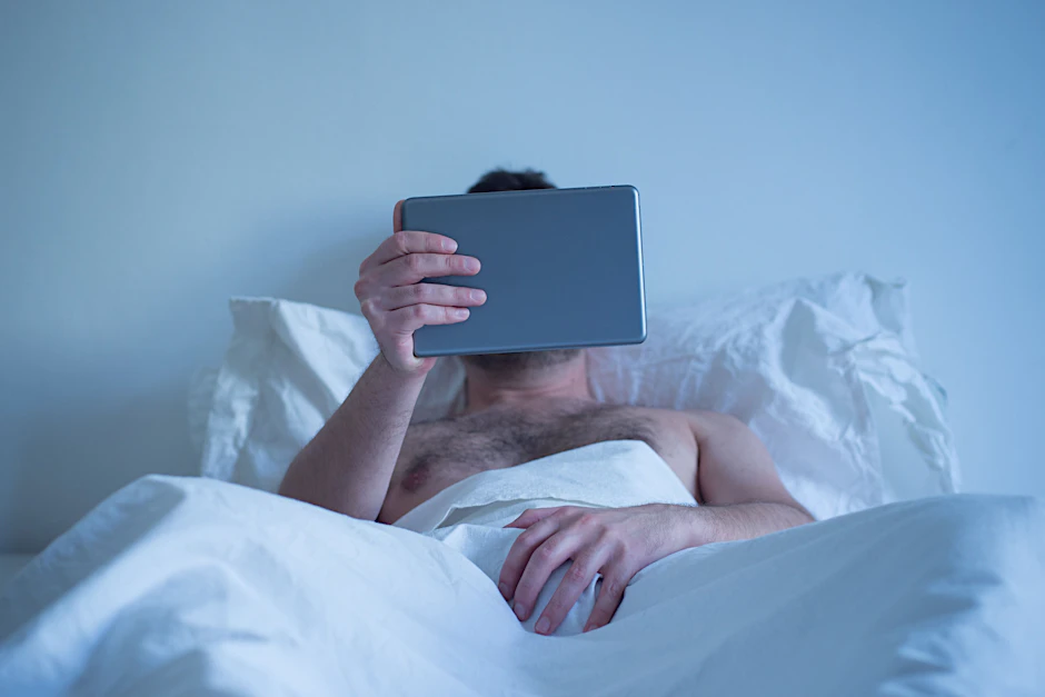 Man lying in the bed , watching porn on the tablet 