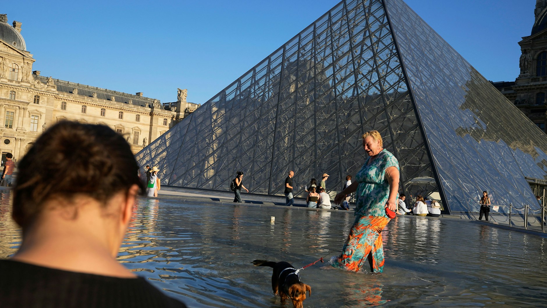 Eine Frau kühlt ihren Hund in einem Springbrunnen neben der Pyramide des Louvre-Museums in Paris.