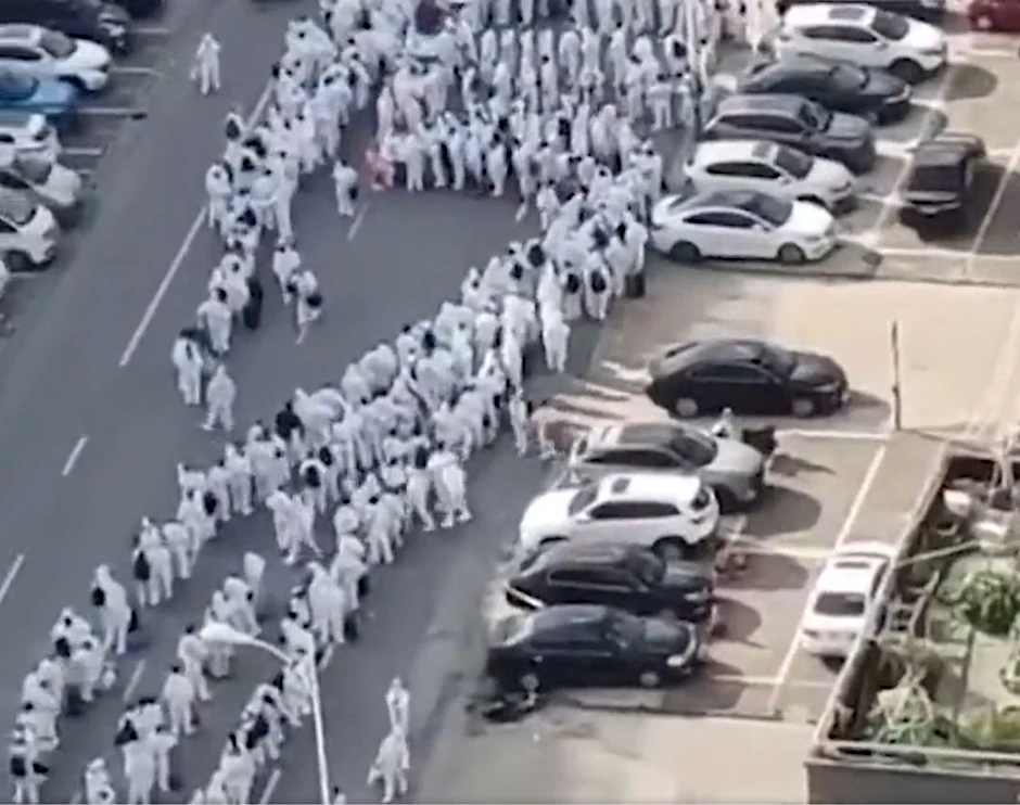 Hunderte Menschen in weißen Schutzanzügen in den Straßen von Wuxi, China.