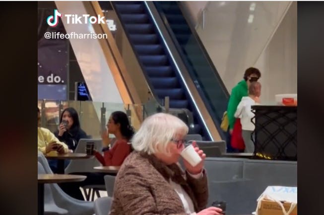 Die Seniorin sitzt in einem Einkaufszentrum und trinkt Kaffee.