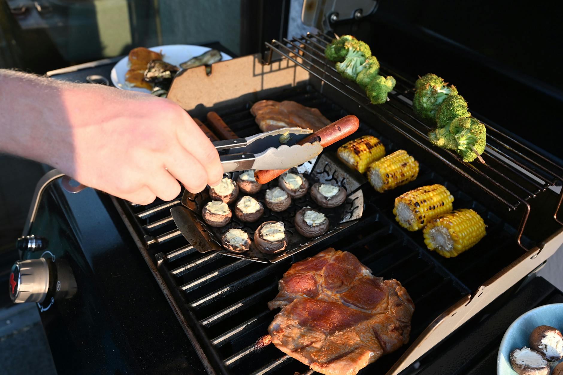 Ein Mann wendet mit einer Zange eine Grillwurst auf einem Gasgrill.