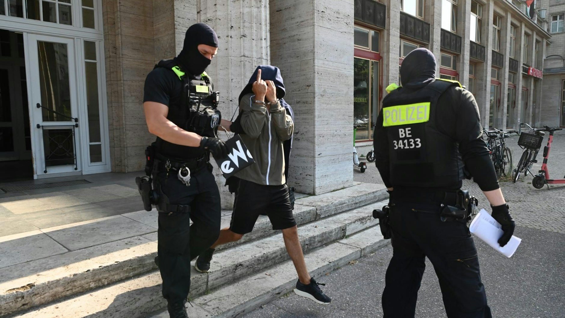 Einer der Verdächtigen wird von Polizisten in der Karl-Marx-Allee abgeführt.