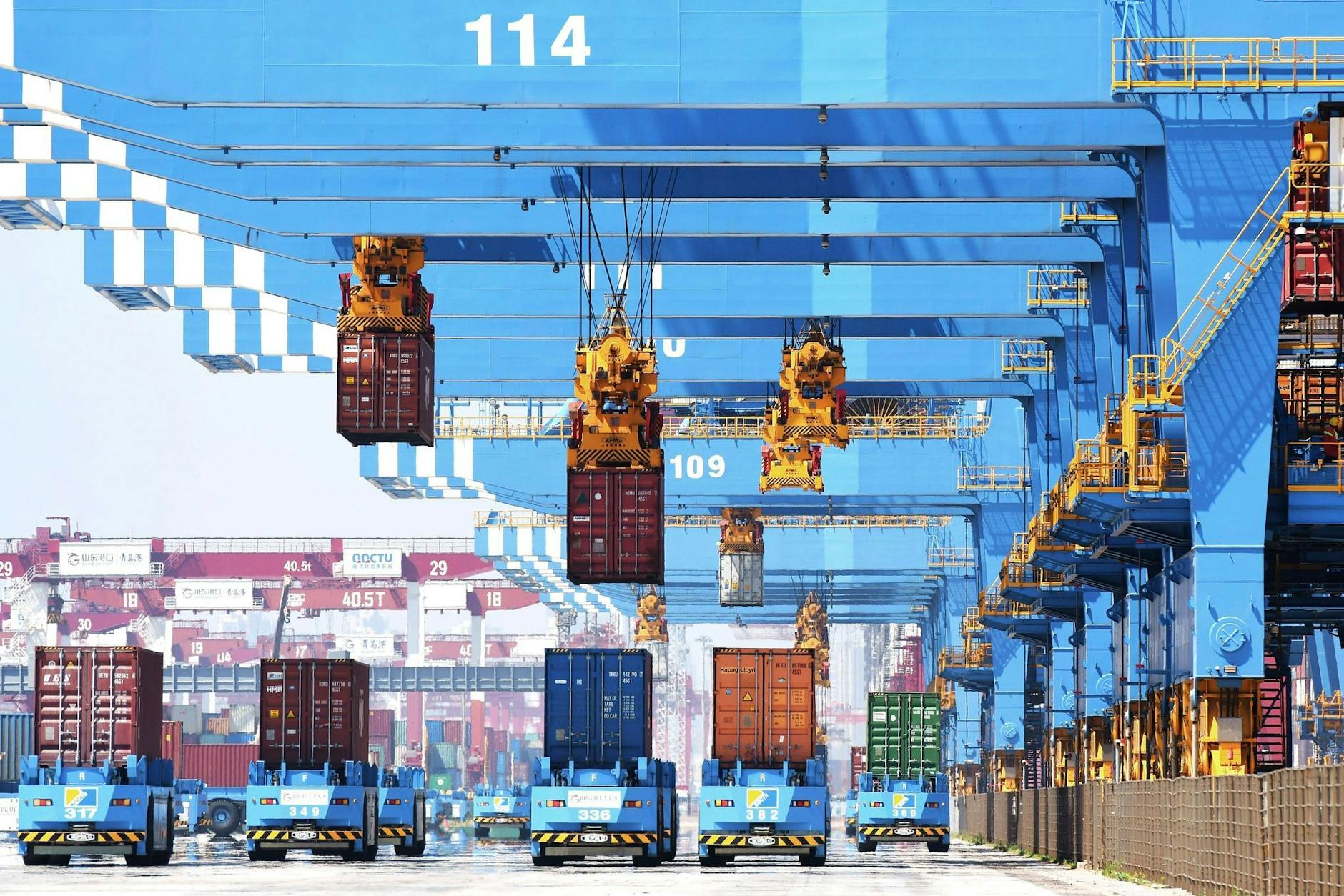 ARCHIV - Kräne bewegen im Hafen von Qingdao im Osten Chinas Container auf Transporter.  