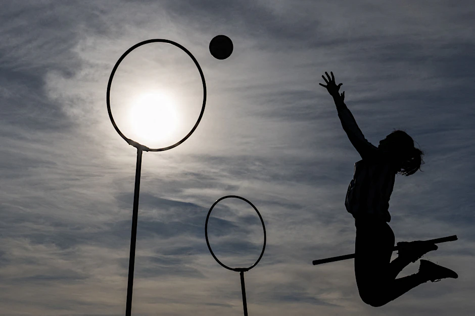 Eine Person vor dämmerndem Himmel schlägt einen Ball durch ein Tor. Sie spielt: „Quadball“.