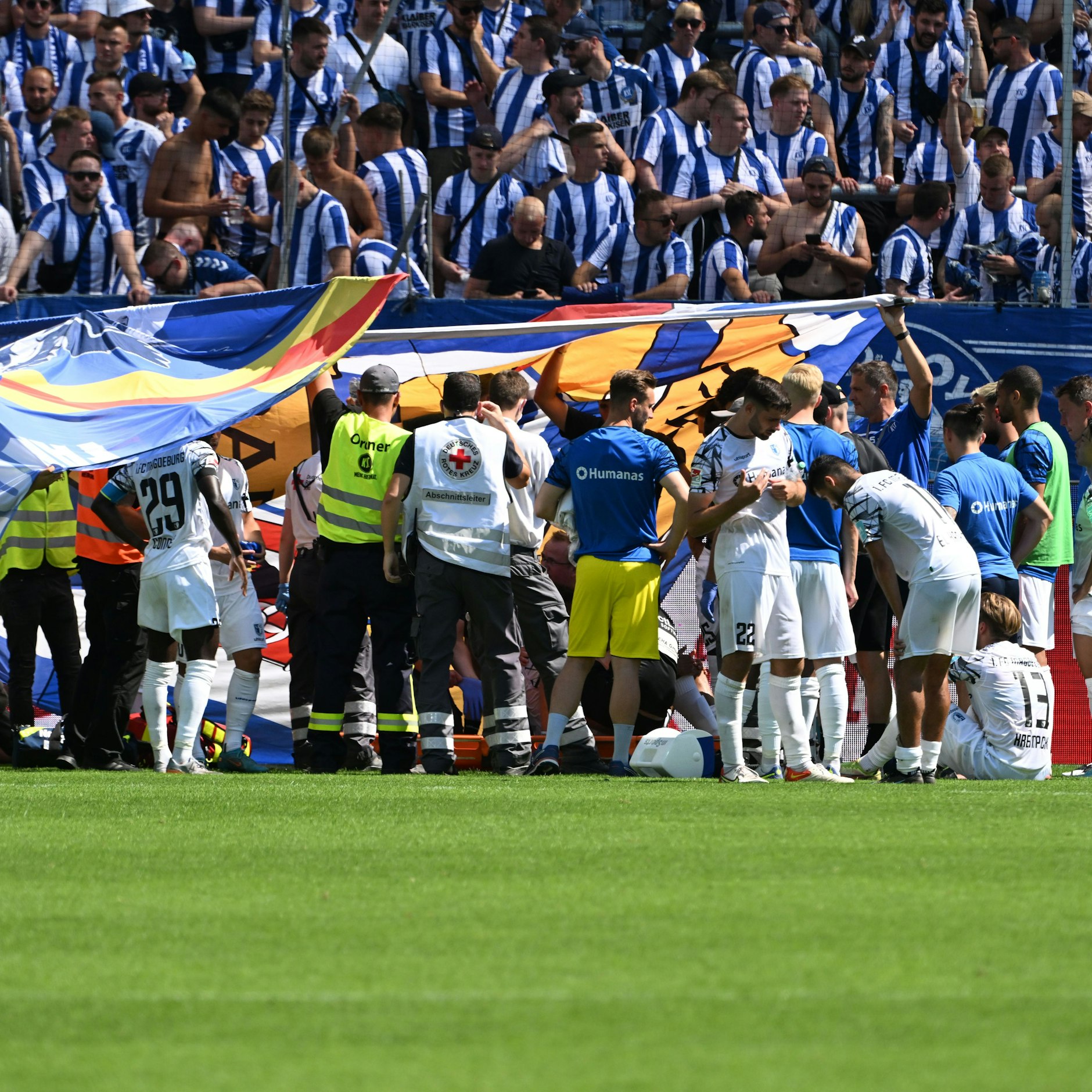 Abgeschirmt durch ein Spalier von Spielern und mit großen KSC-Bannern wird&nbsp; nach Spielende Magdeburgs&nbsp; Jamie Lawrence auf dem Platz behandelt und in einer Trage vom Platz befördert.