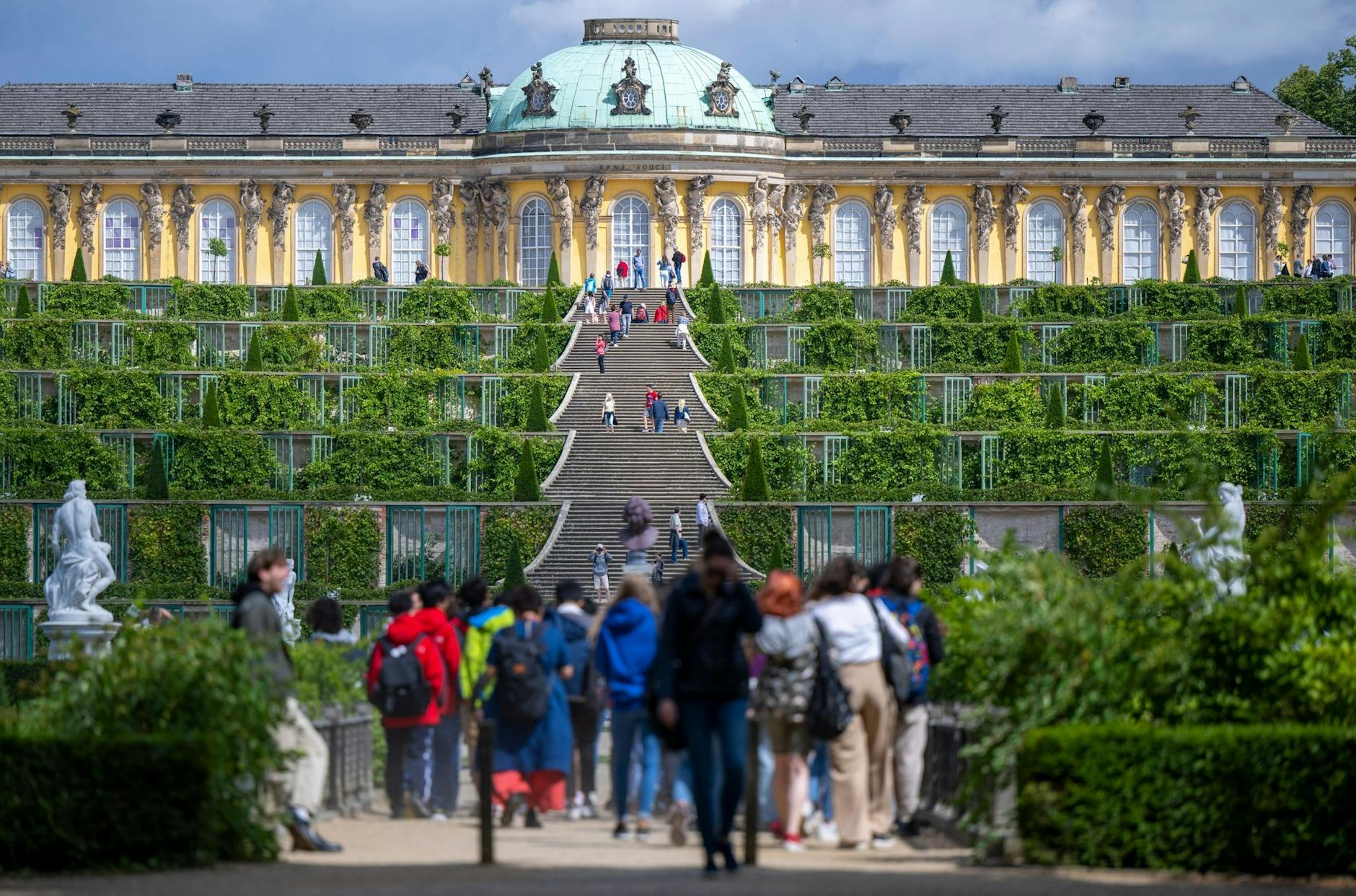 Zahlreiche Besucher spazieren bei sonnigem Wetter im Park Sanssouci auf das Schloss zu. d
