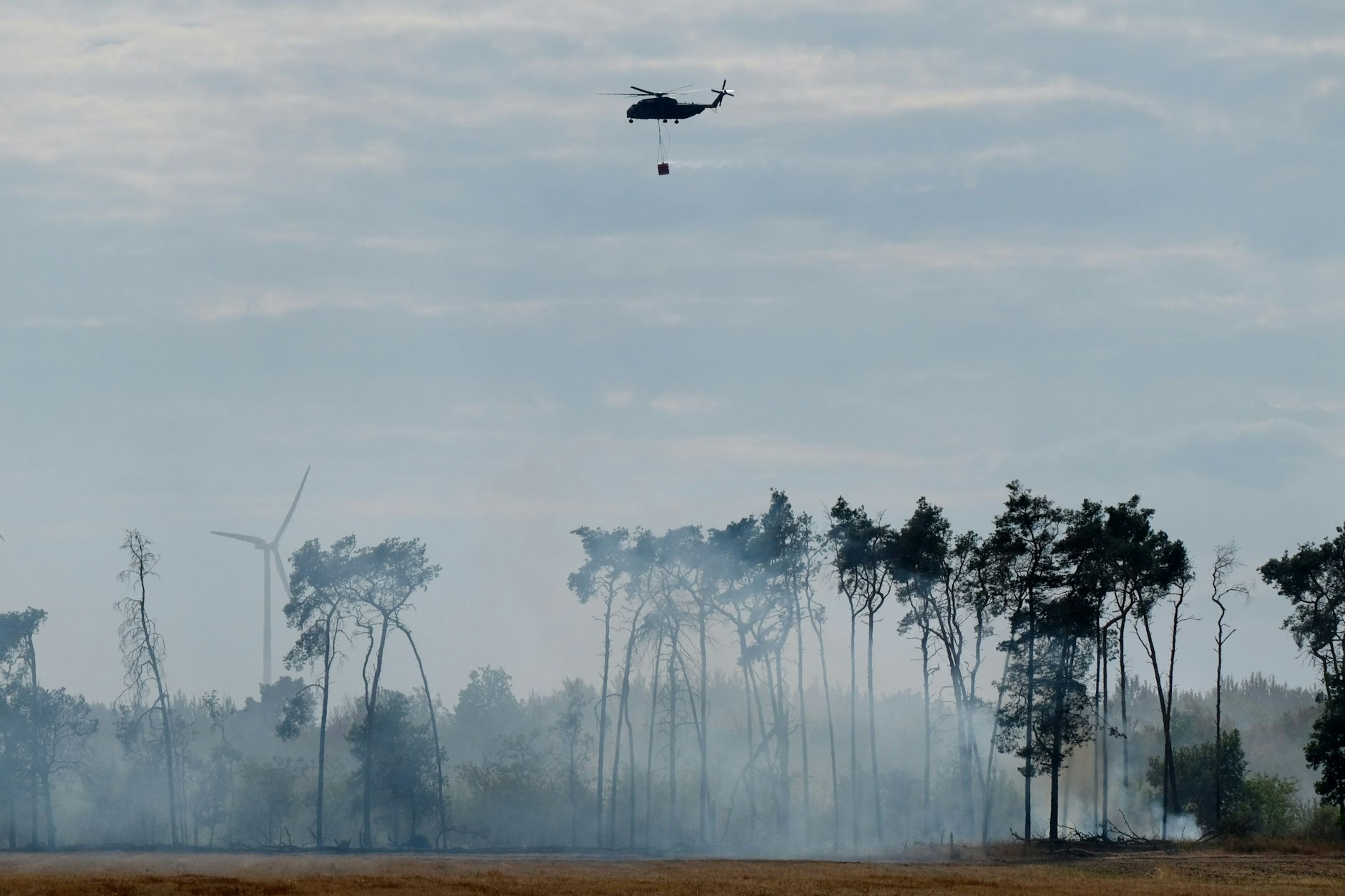 Ein Hubschrauber mit Wasserbehälter fliegt über den Waldbrand im Landkreis Elbe-Elster.