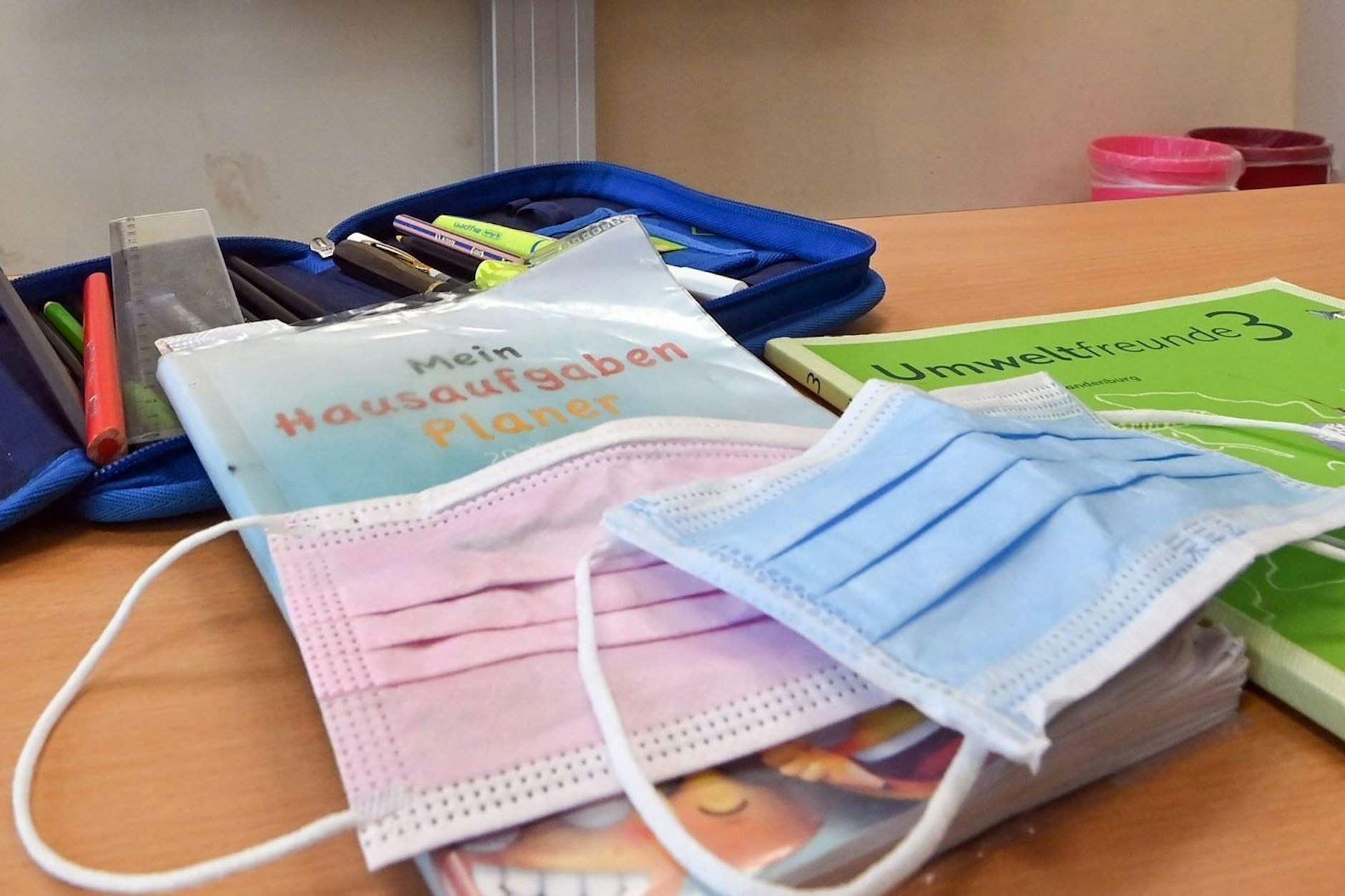 Corona-Masken liegen in einem Klassenzimmer auf einem Schulbuch. (Symbolbild)