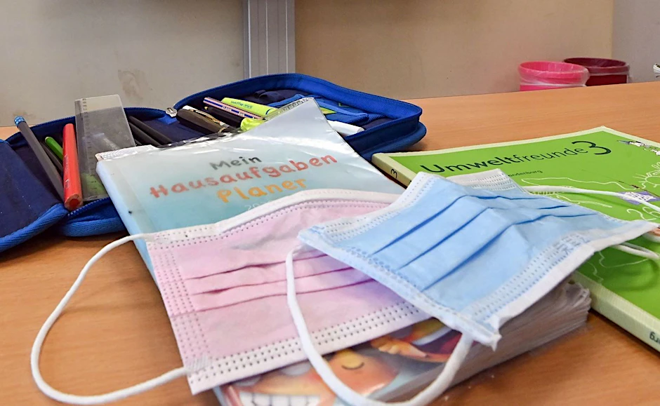 Corona-Masken liegen in einem Klassenzimmer auf einem Schulbuch. (Symbolbild)