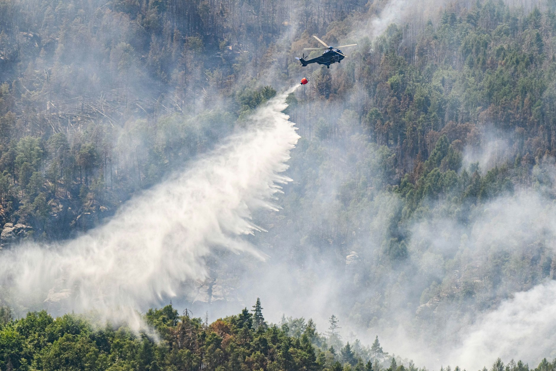 Ein Hubschrauber der Bundespolizei fliegt mit einem Löschwasser-Außenlastbehälter, um einen Waldbrand im Nationalpark Sächsische Schweiz zu löschen.