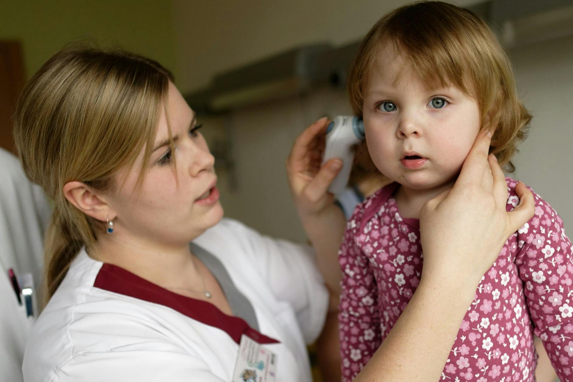 Eine Kinderärztin misst bei einer kleinen Patientin im Ohr die Körpertemperatur.