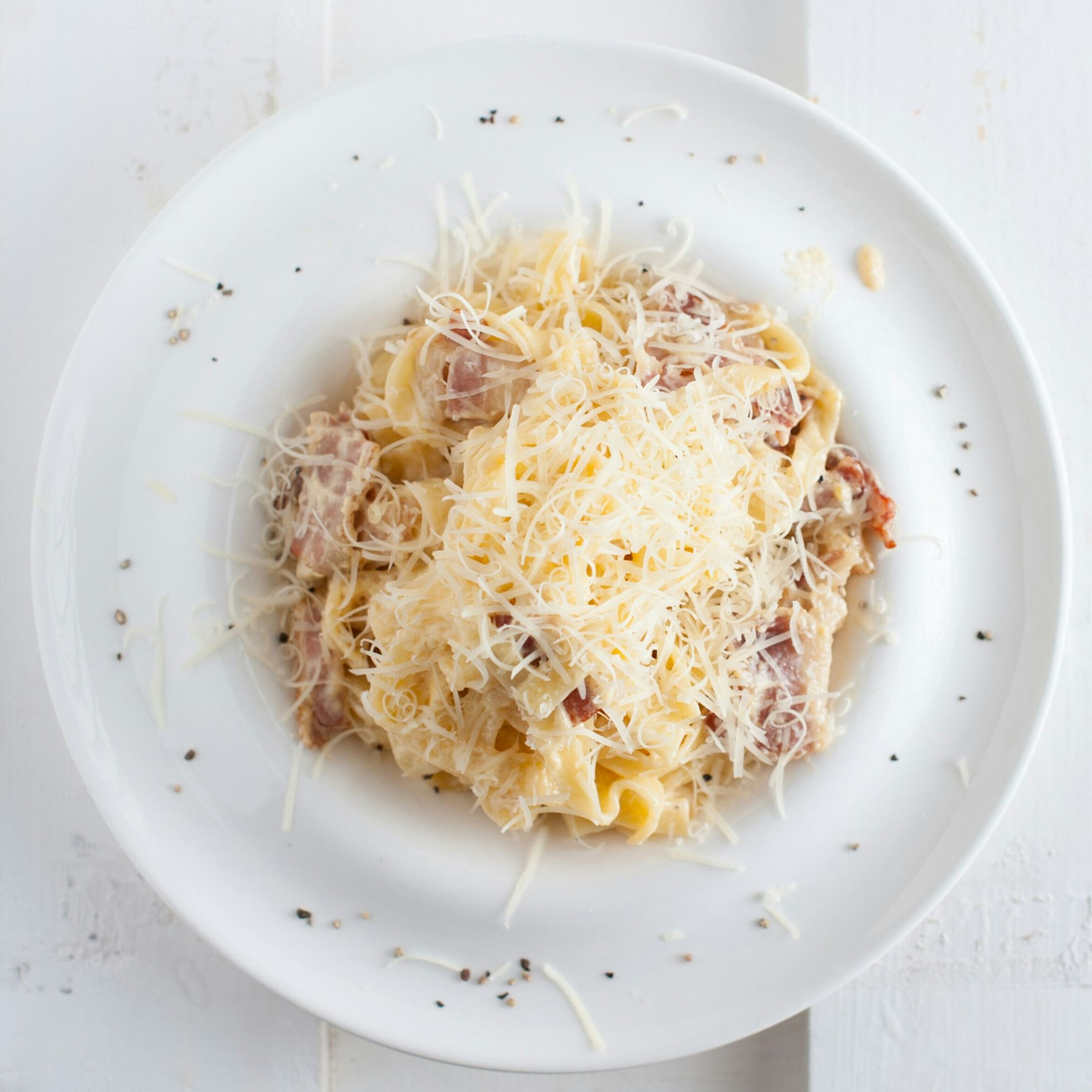Spaghetti Carbonara wird mit geriebenem Parmesan und frischem Pfeffer bestreut und serviert.