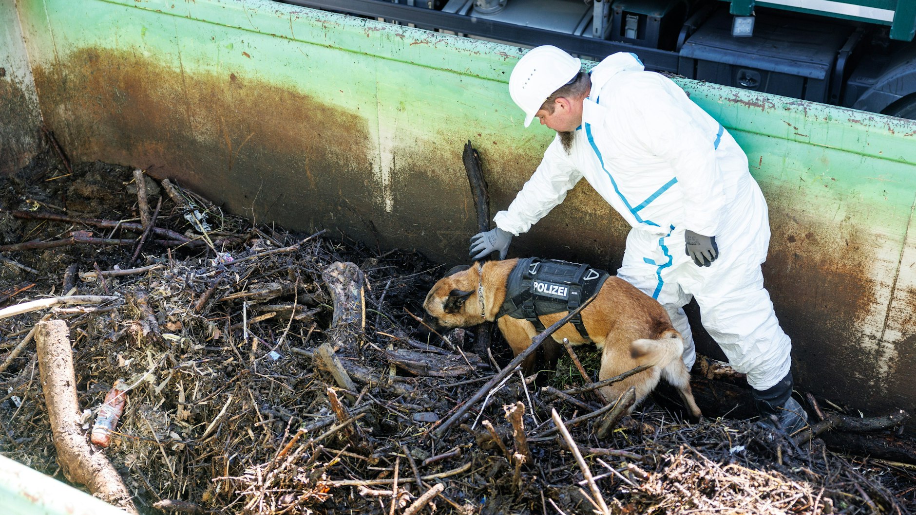 Nach dem Fund der Kinderleiche: Ein Polizist durchsucht mit einem Spürhund einen Container mit Treibgut.