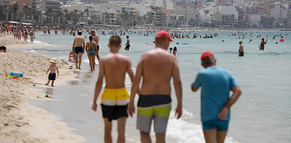 ARCHIV - Menschen laufen am Strand von Arenal auf Mallorca.  