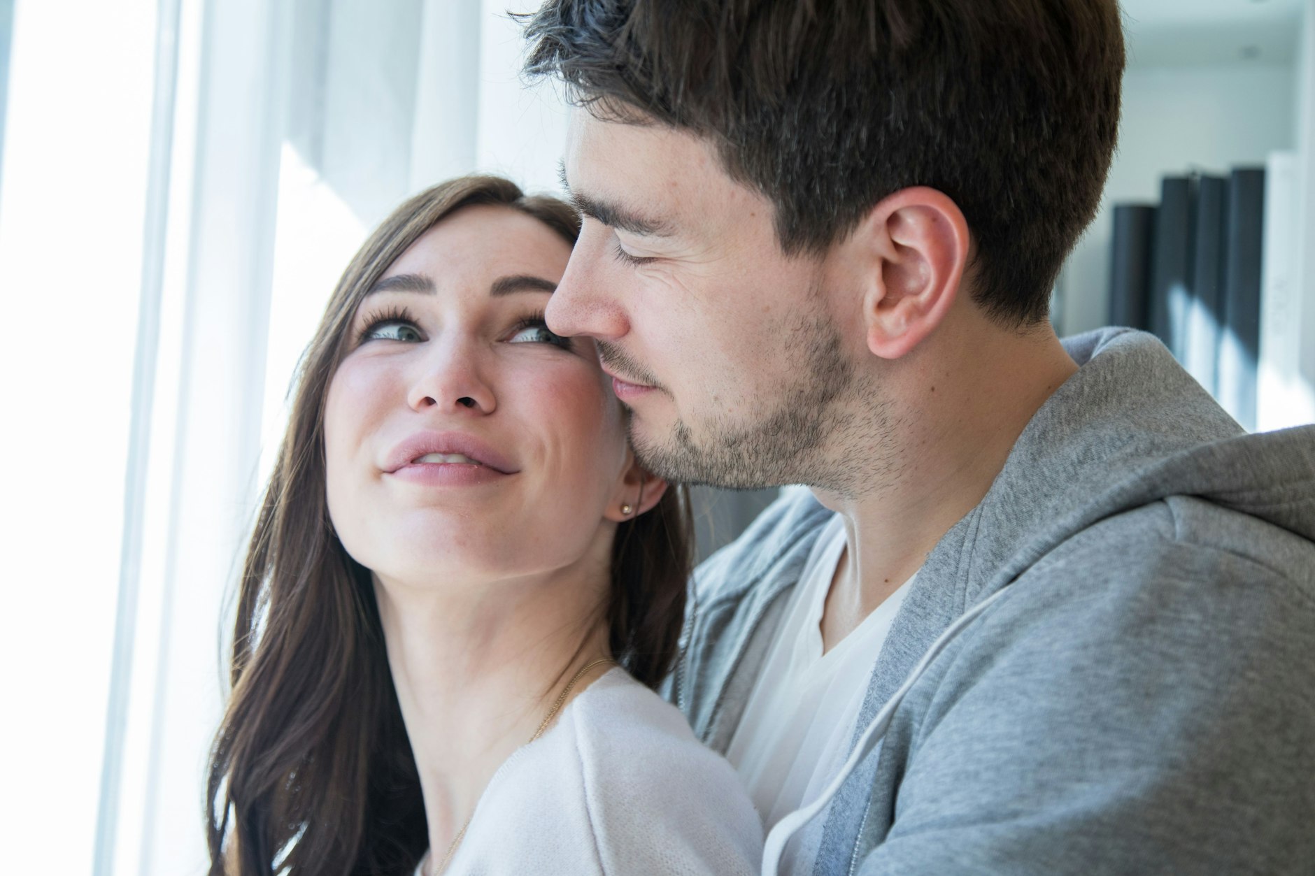 ILLUSTRATION - Ein junges Paar steht umschlungen am Fenster.