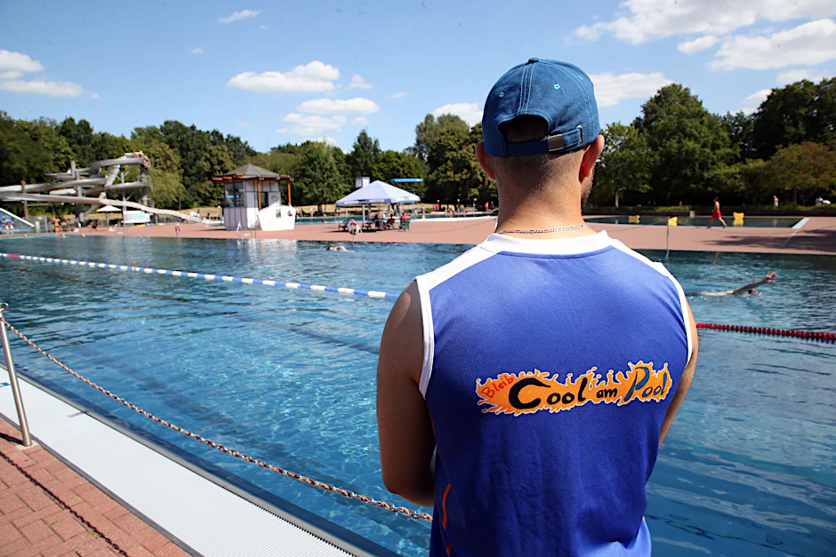 Ein Mitglied des Projekts Cool am Pool beobachtet vom Beckenrand im Sommerbad Pankow das Badegeschehen.