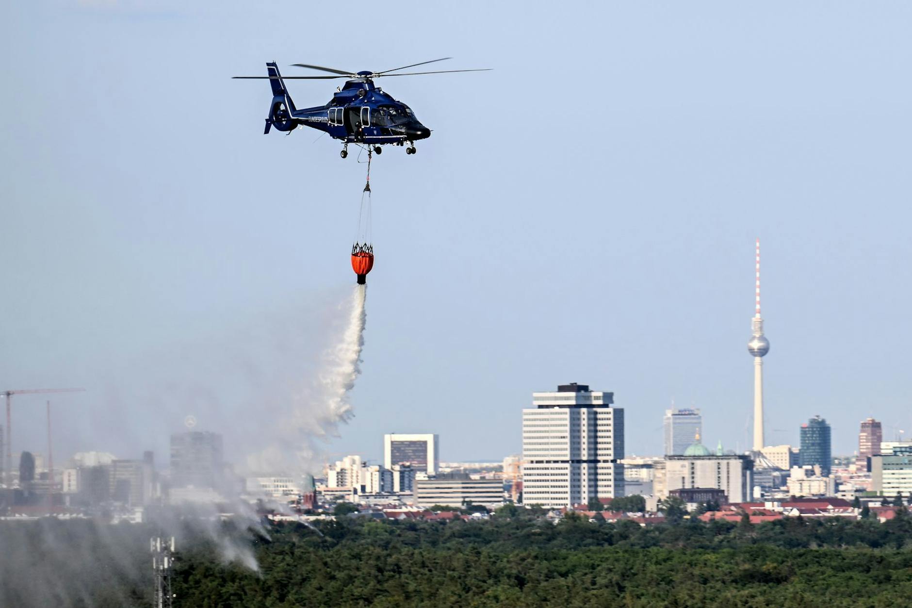 Ein Hubschrauber der Bundespolizei wirft Wasser über der Brandstelle im Grunewald ab.