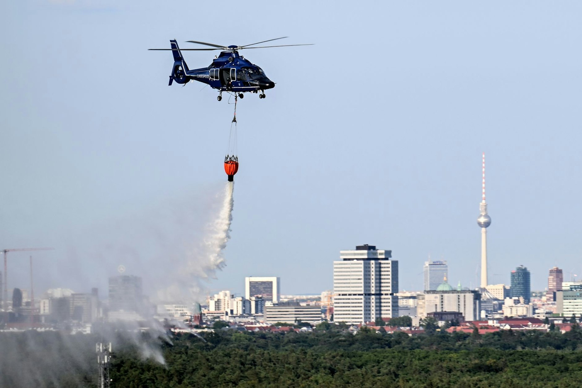 Ein Hubschrauber der Bundespolizei wirft Wasser über der Brandstelle im Grunewald ab.